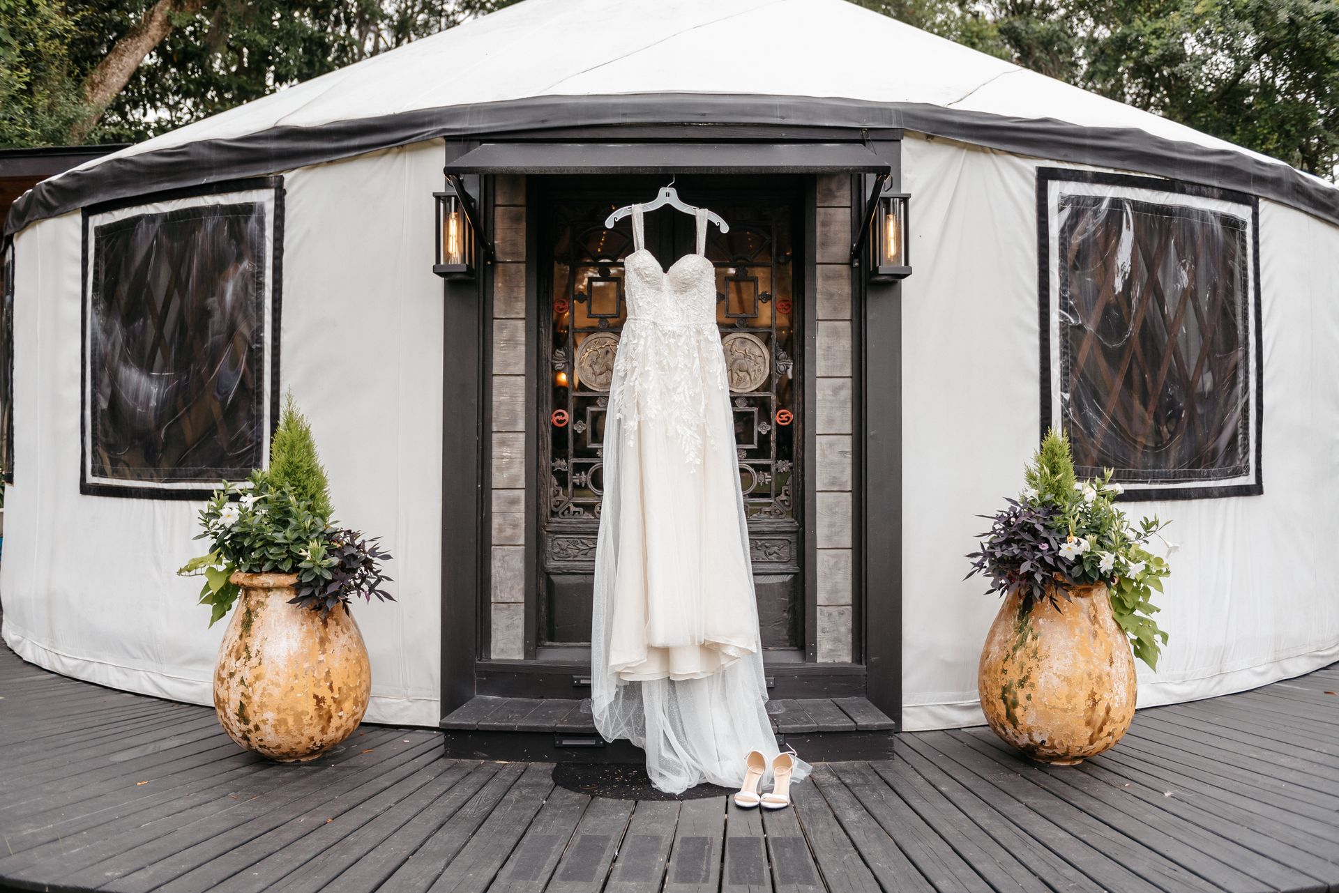 White wedding dress hanging in a doorway of a white event tent with potted plants on either side