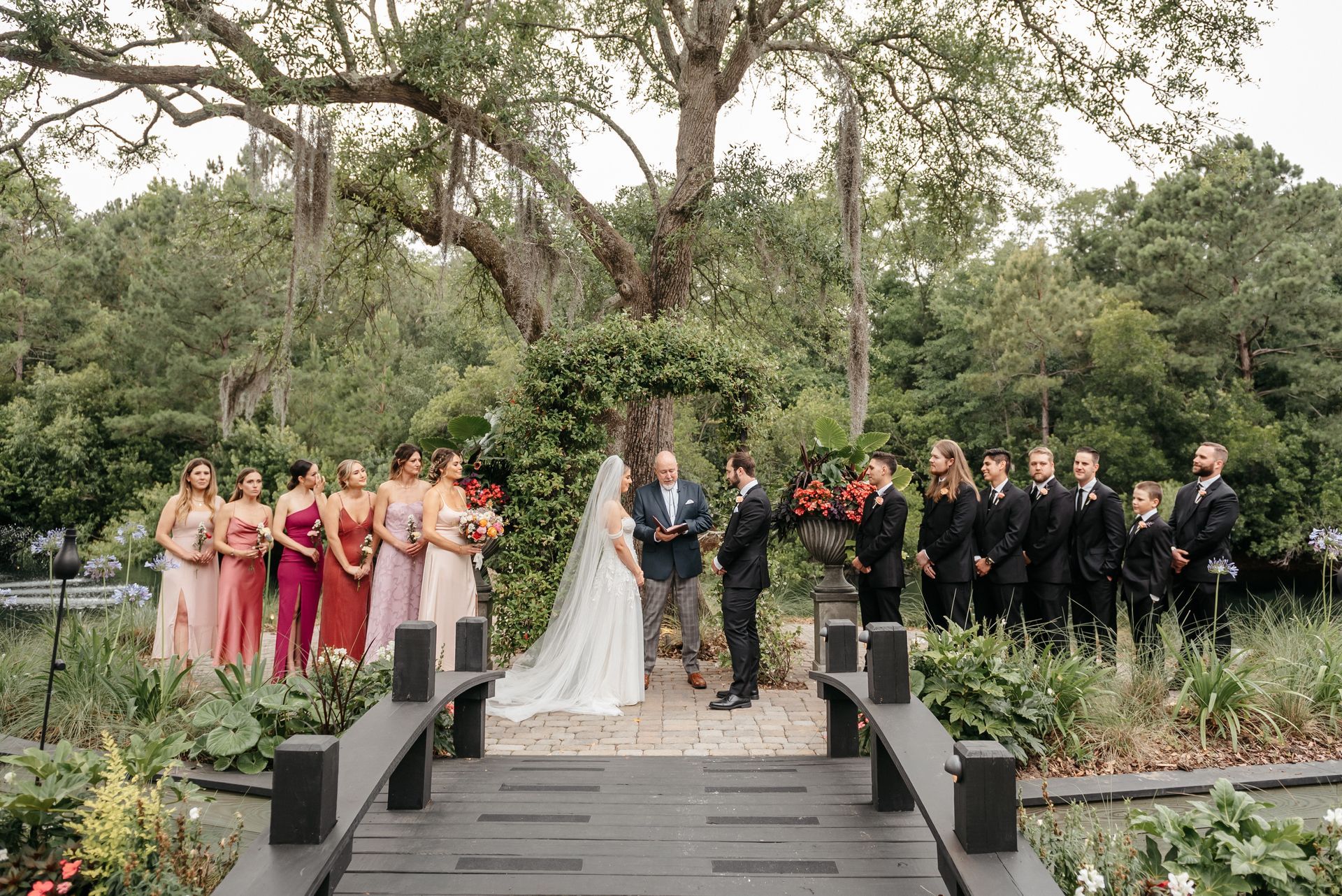 Wedding party posed on garden steps with bride, groom, bridesmaids, and groomsmen amid greenery