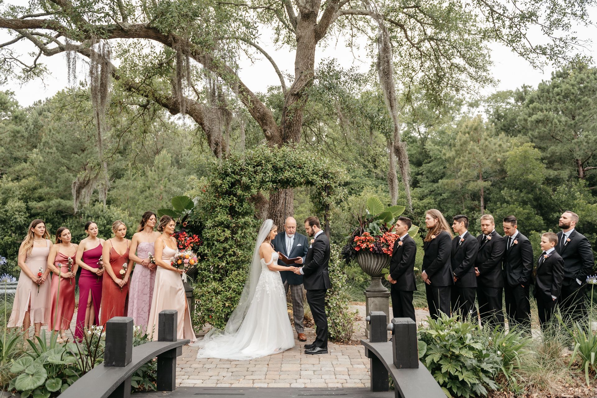 Wedding ceremony in a garden with bride, groom, wedding party, and officiant on a decorated stone path