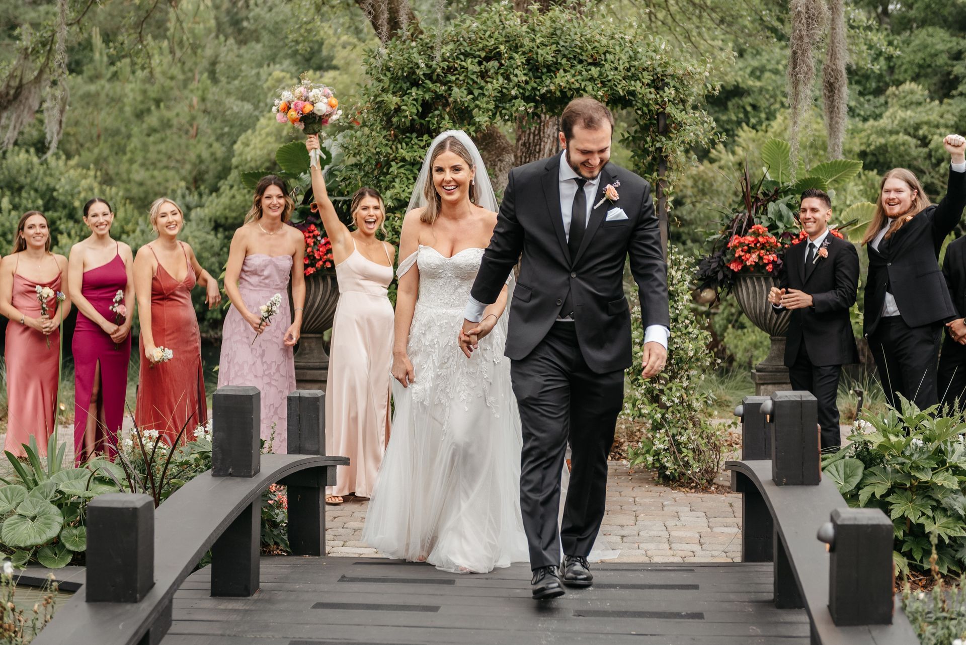 Newlyweds walking down an outdoor aisle, surrounded by wedding party and guests in formal attire