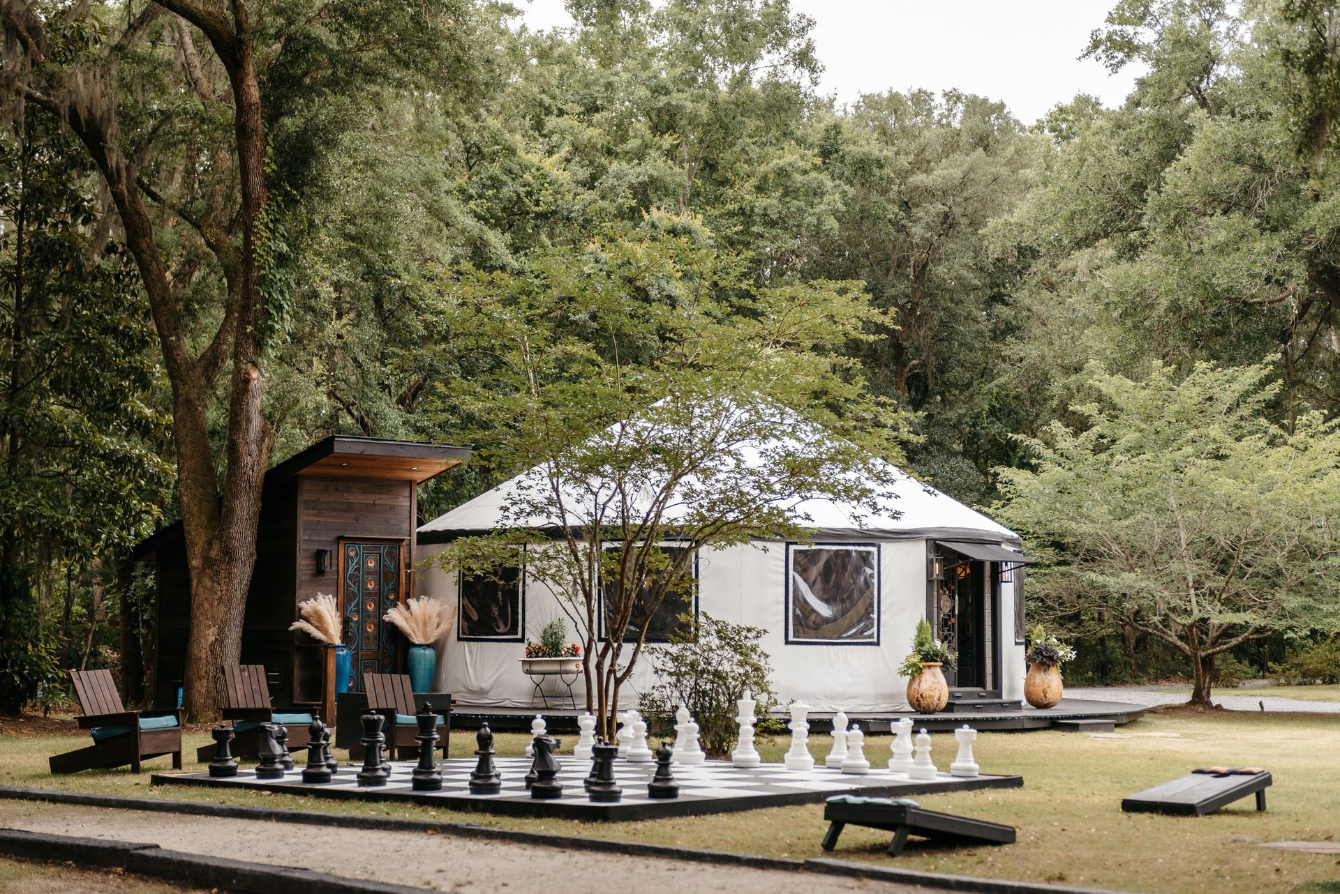 White yurt-style tent in a wooded campsite with people standing on a deck and folding chairs nearby