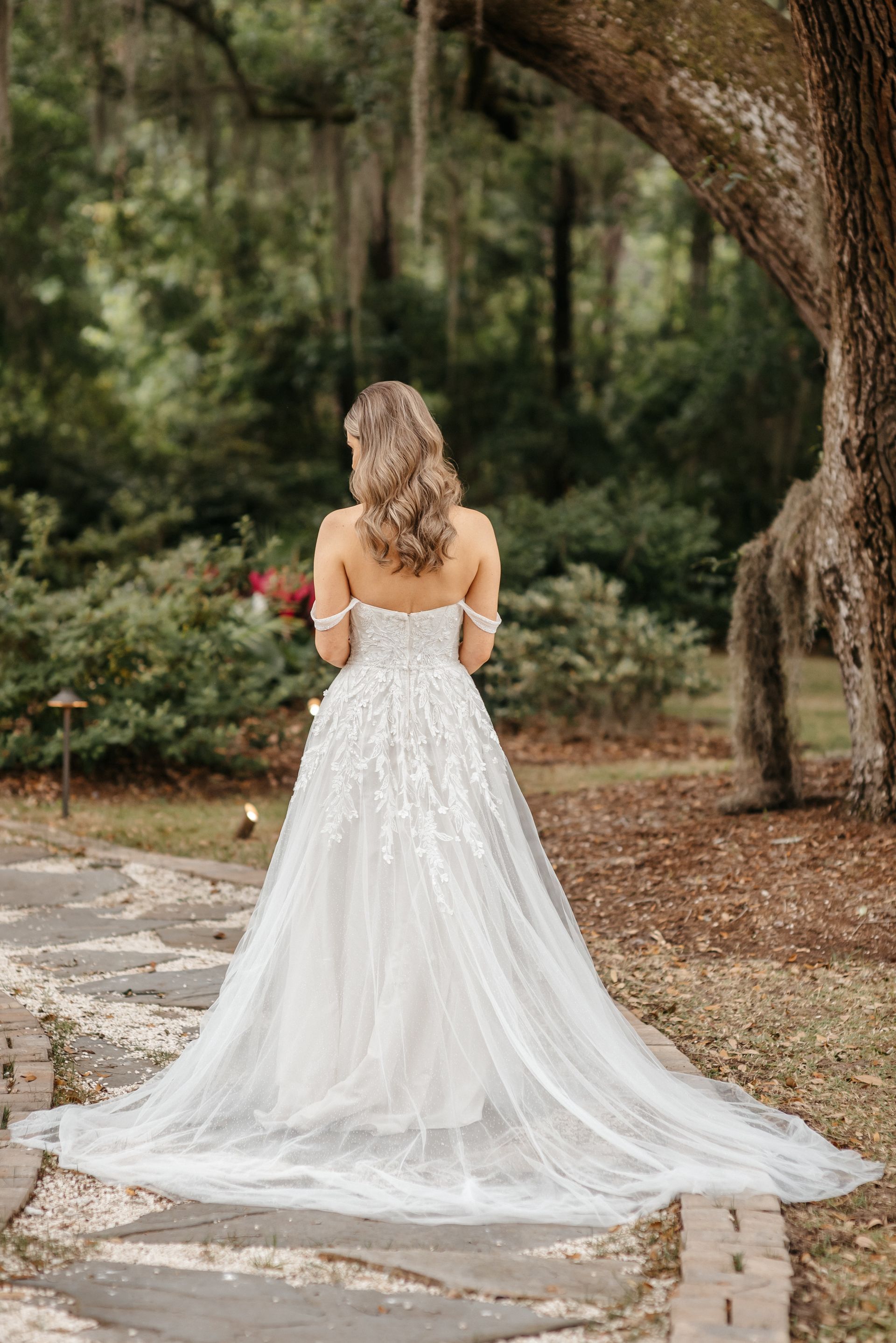 Woman in a white wedding gown standing on a stone path in a wooded garden