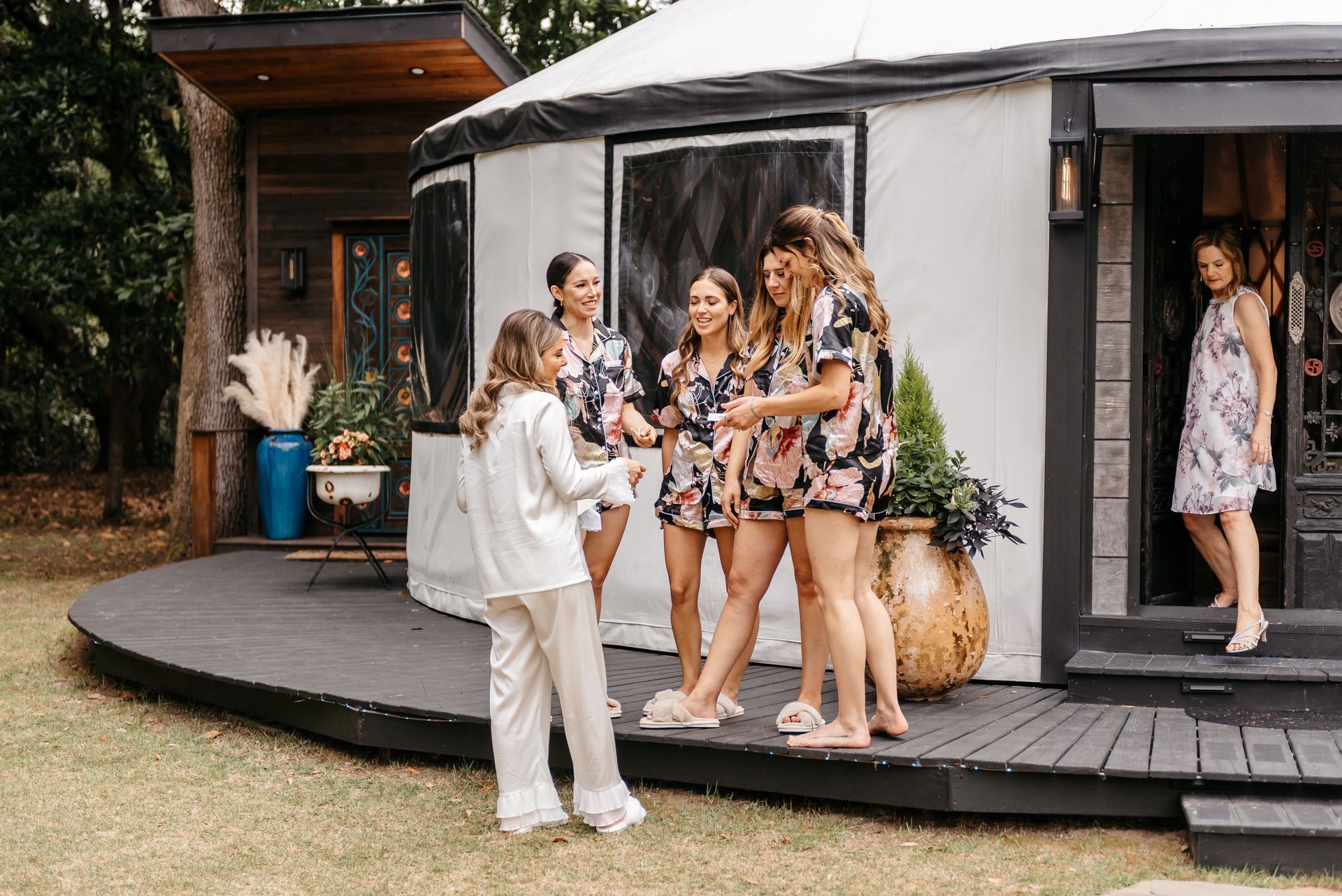 Group chatting on a porch outside a modern house, with one person holding papers.