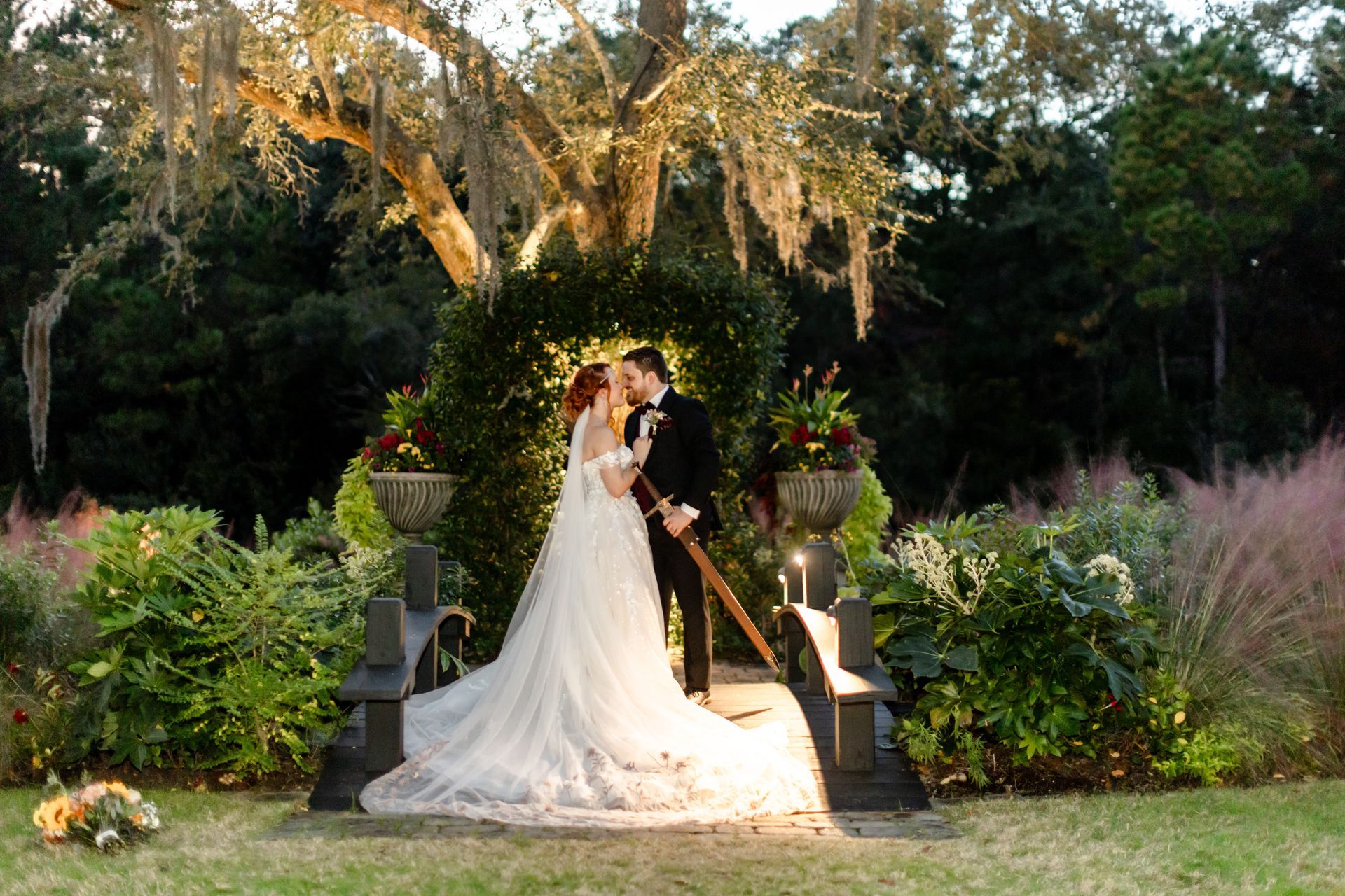 Bride and groom kissing on a garden altar under hanging greenery, surrounded by flowers at dusk
