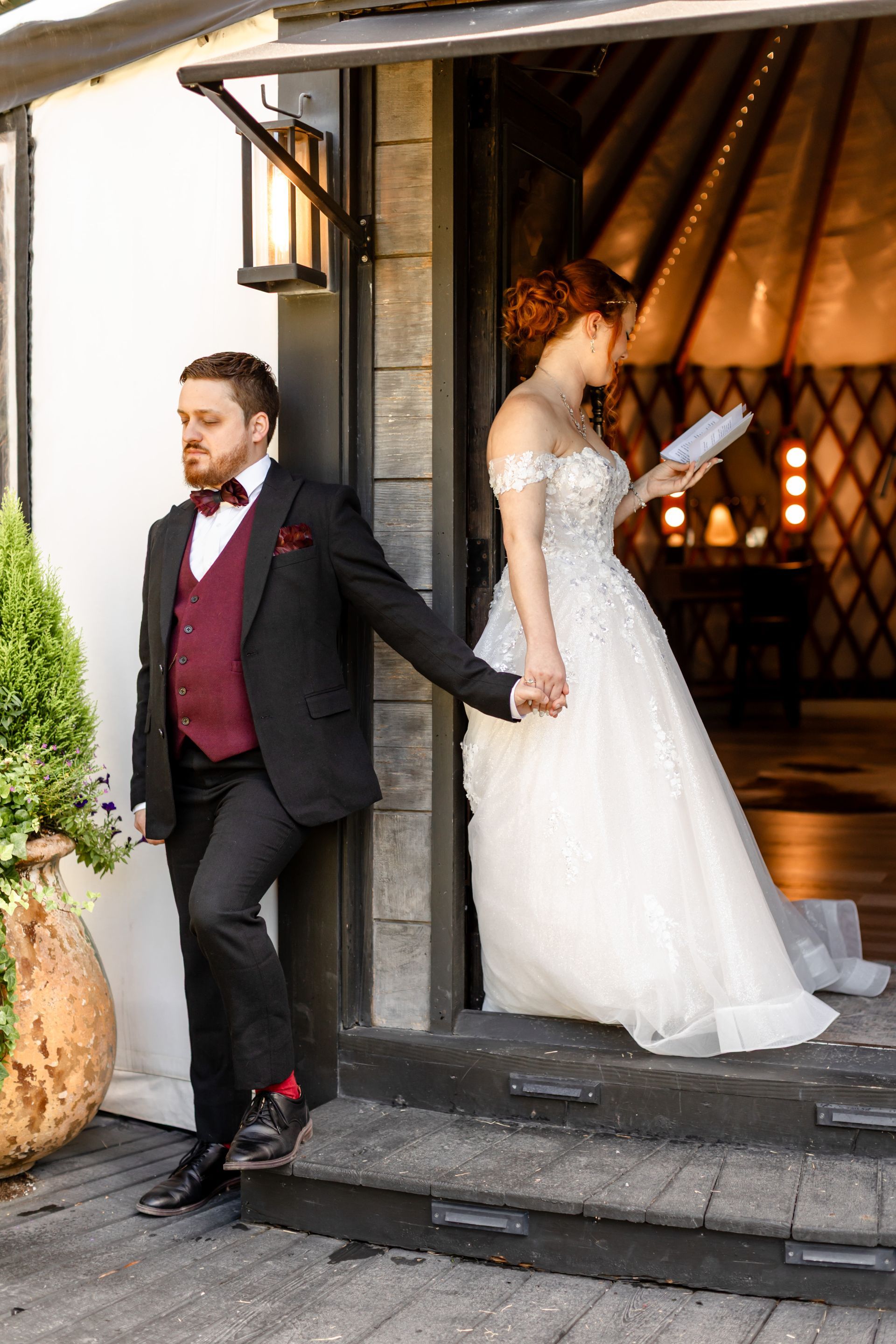 Wedding couple holding hands at a doorway, groom in dark suit and bride in white gown with bouquet