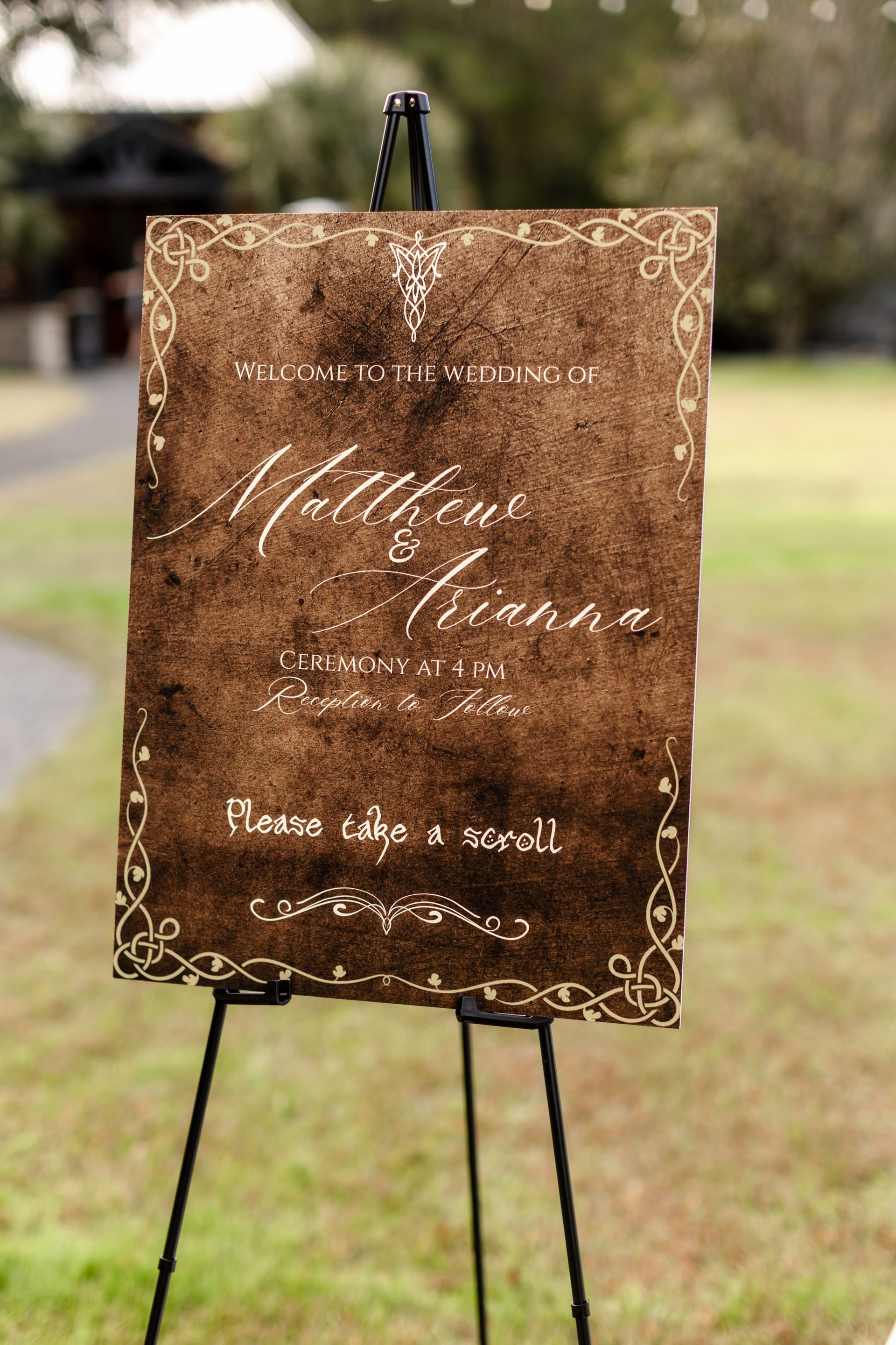 Rustic brown wedding sign on a black easel in a grassy outdoor setting