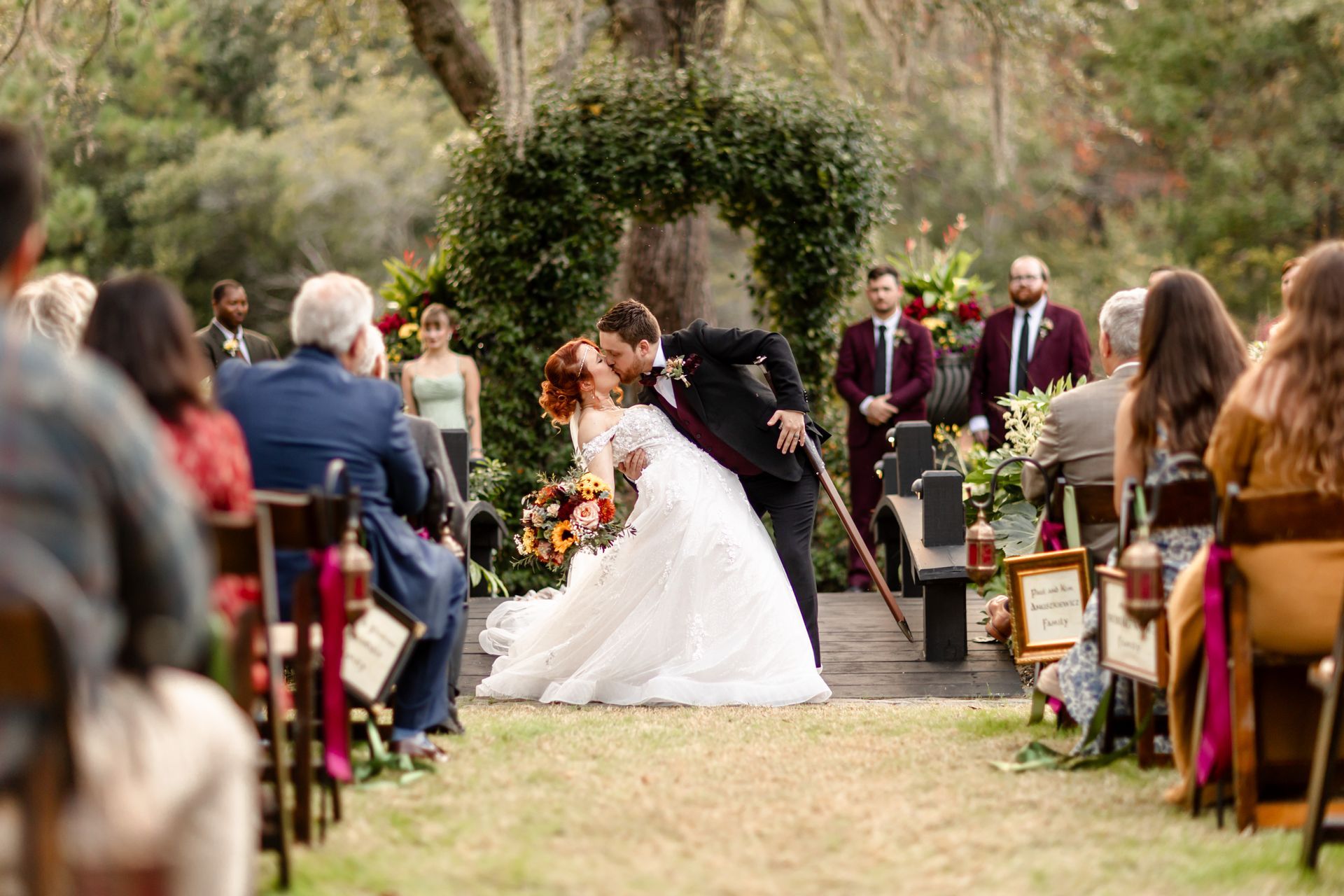 Bride and groom kissing outdoors during a garden wedding ceremony, guests seated on both sides