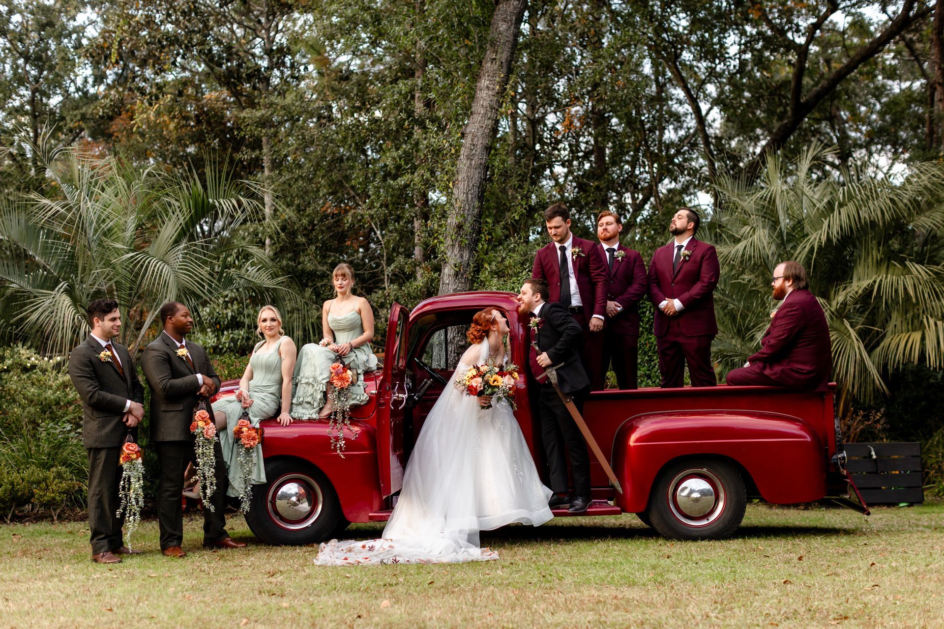 Wedding party posing on a red vintage pickup truck in a grassy outdoor setting