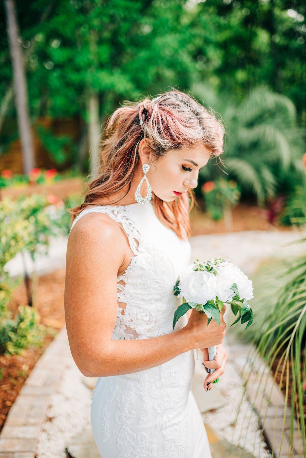 Bride in a white lace dress holding a bouquet on a garden path