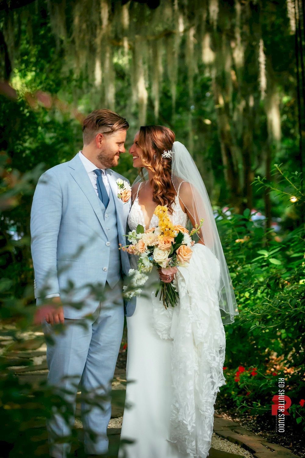 Bride and groom in light-colored attire sharing a moment in a lush garden setting