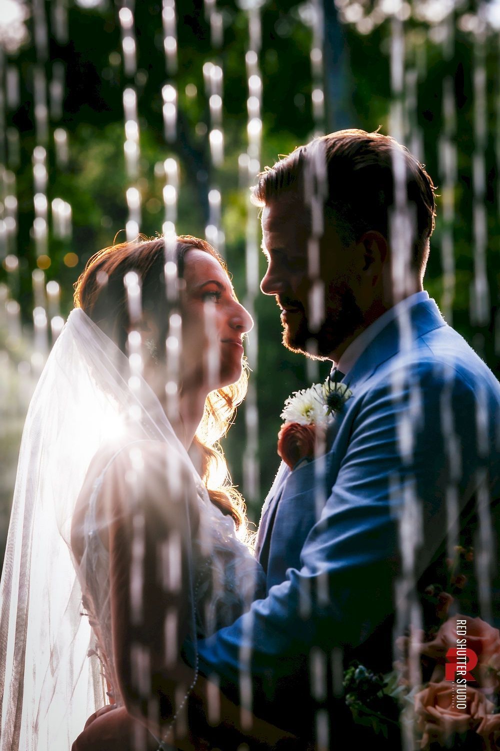 Couple exchanging vows under a waterfall spray, with a white veil and blue suit.