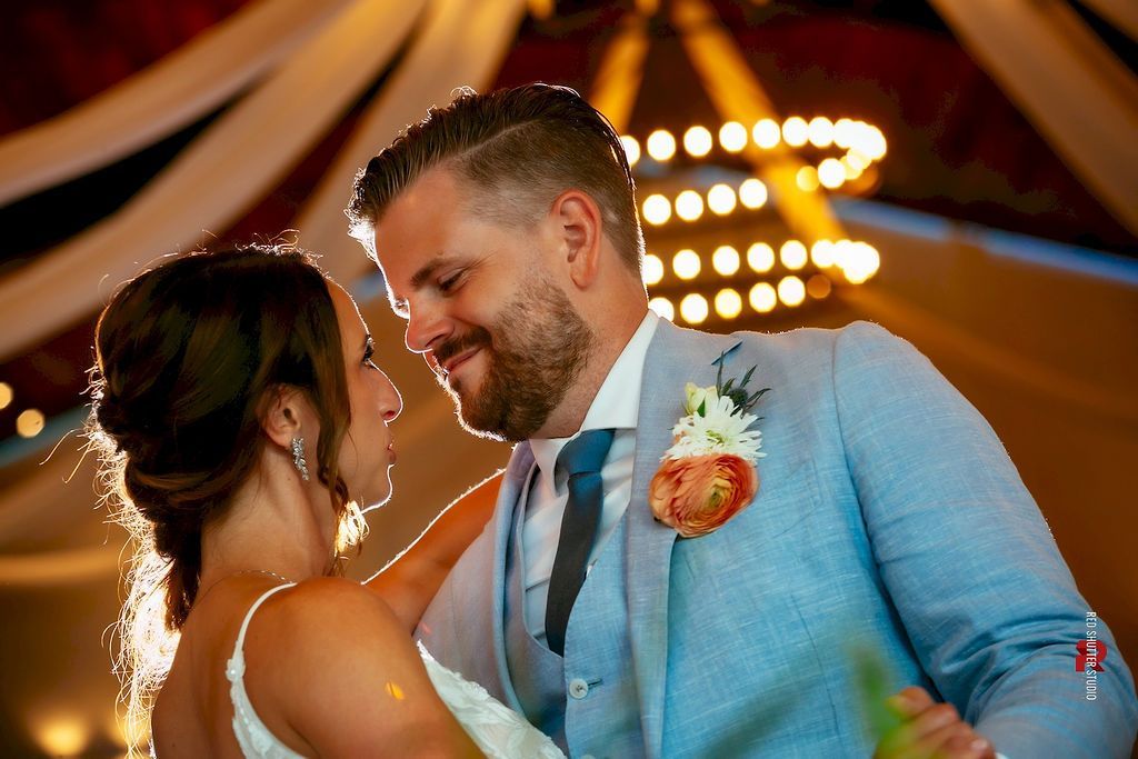 Couple dancing closely at a warmly lit wedding reception, smiling and facing each other.