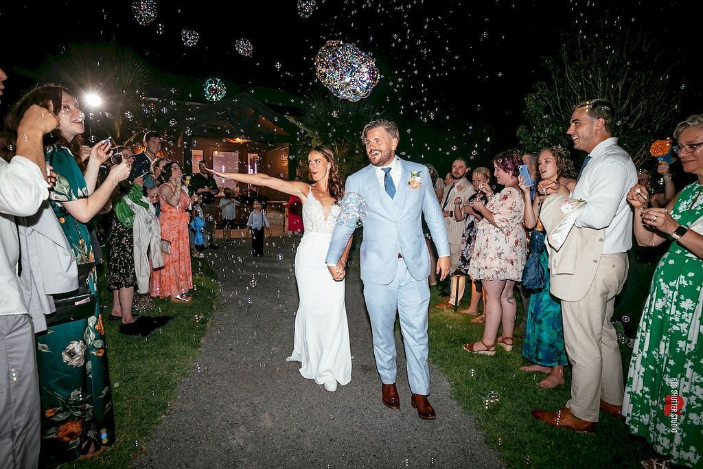 Newlyweds celebrating outdoors at night, walking under falling confetti with guests applauding on both sides.
