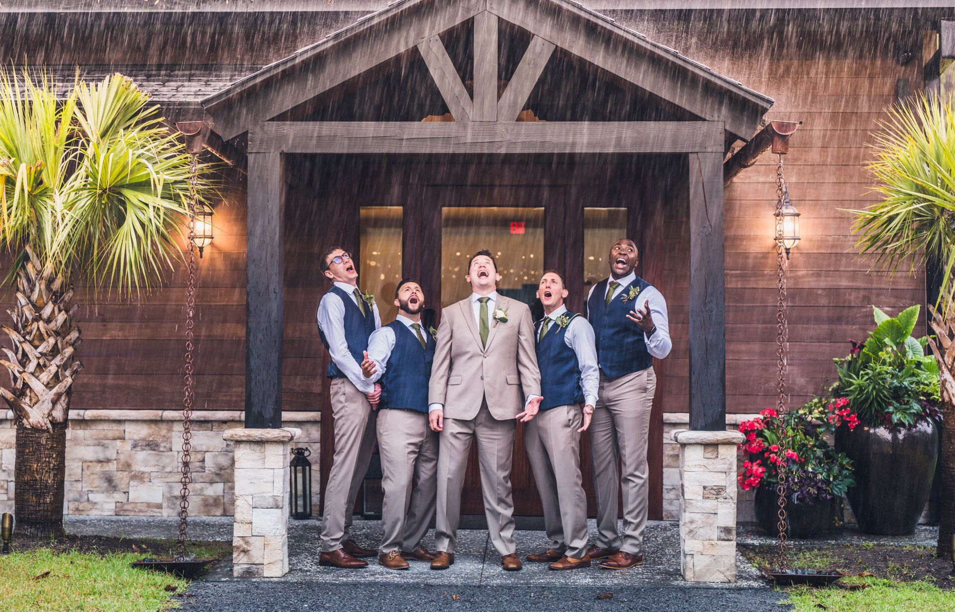 Five people posing outside a rustic wooden building in the rain, one holding a bouquet.