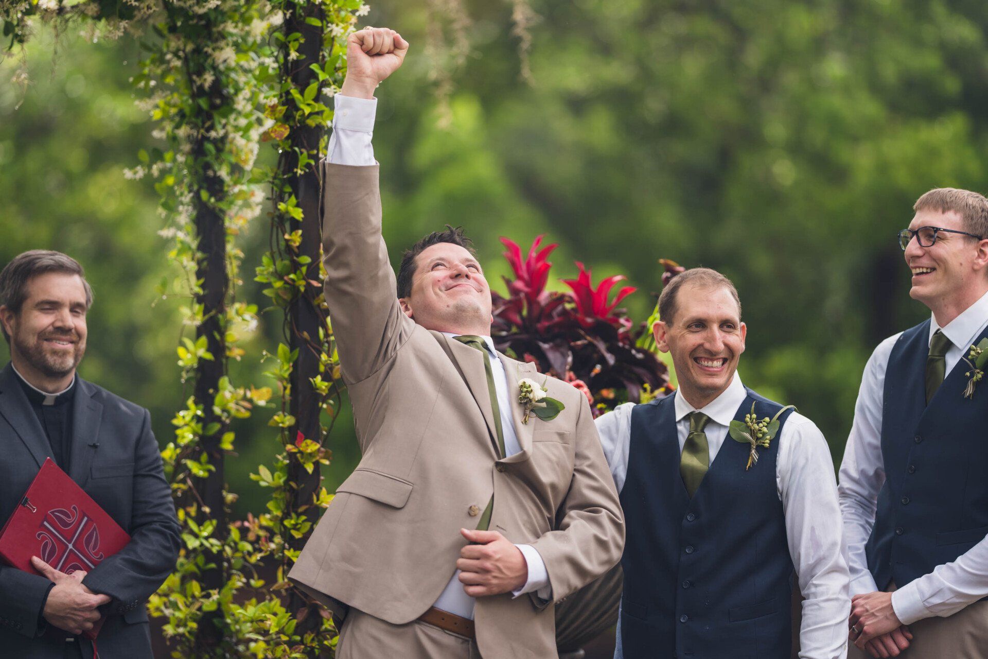Bride and groomsmen celebrating outdoors, one man raising a fist in the air