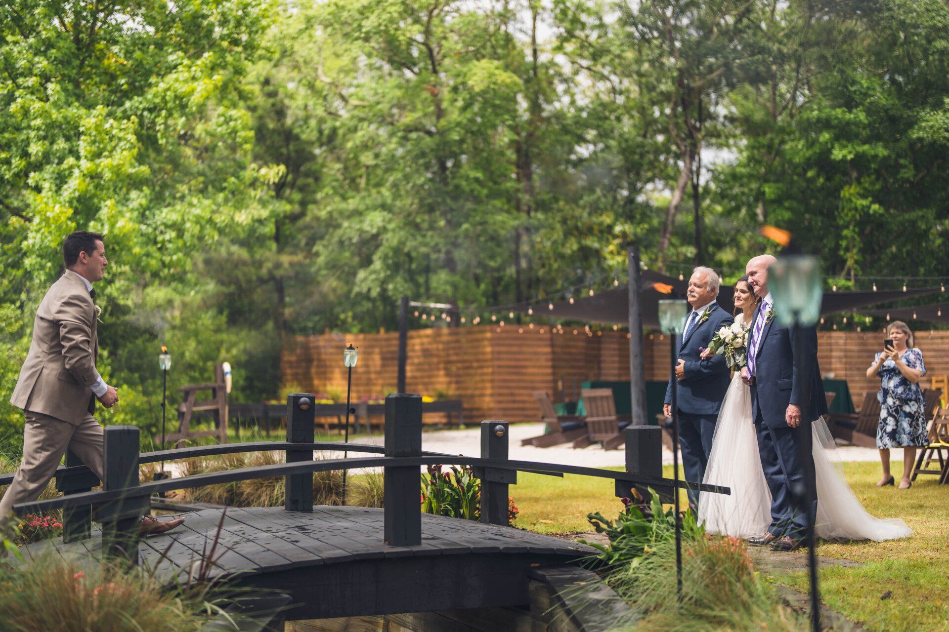 Wedding ceremony by a pond in a lush park, with the couple standing beside an officiant and guests nearby.