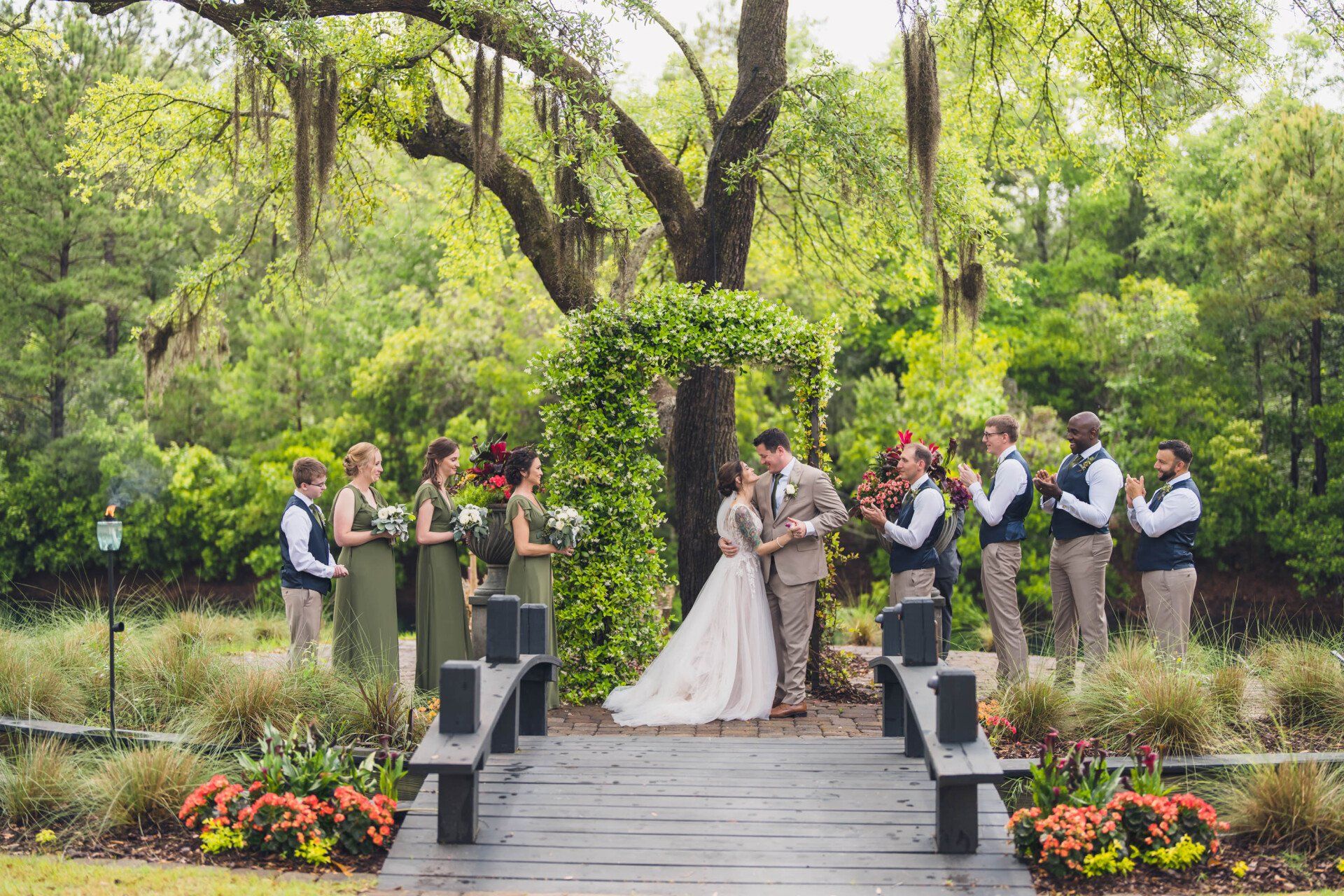 Outdoor wedding ceremony on a garden bridge, with guests standing among flowers and trees