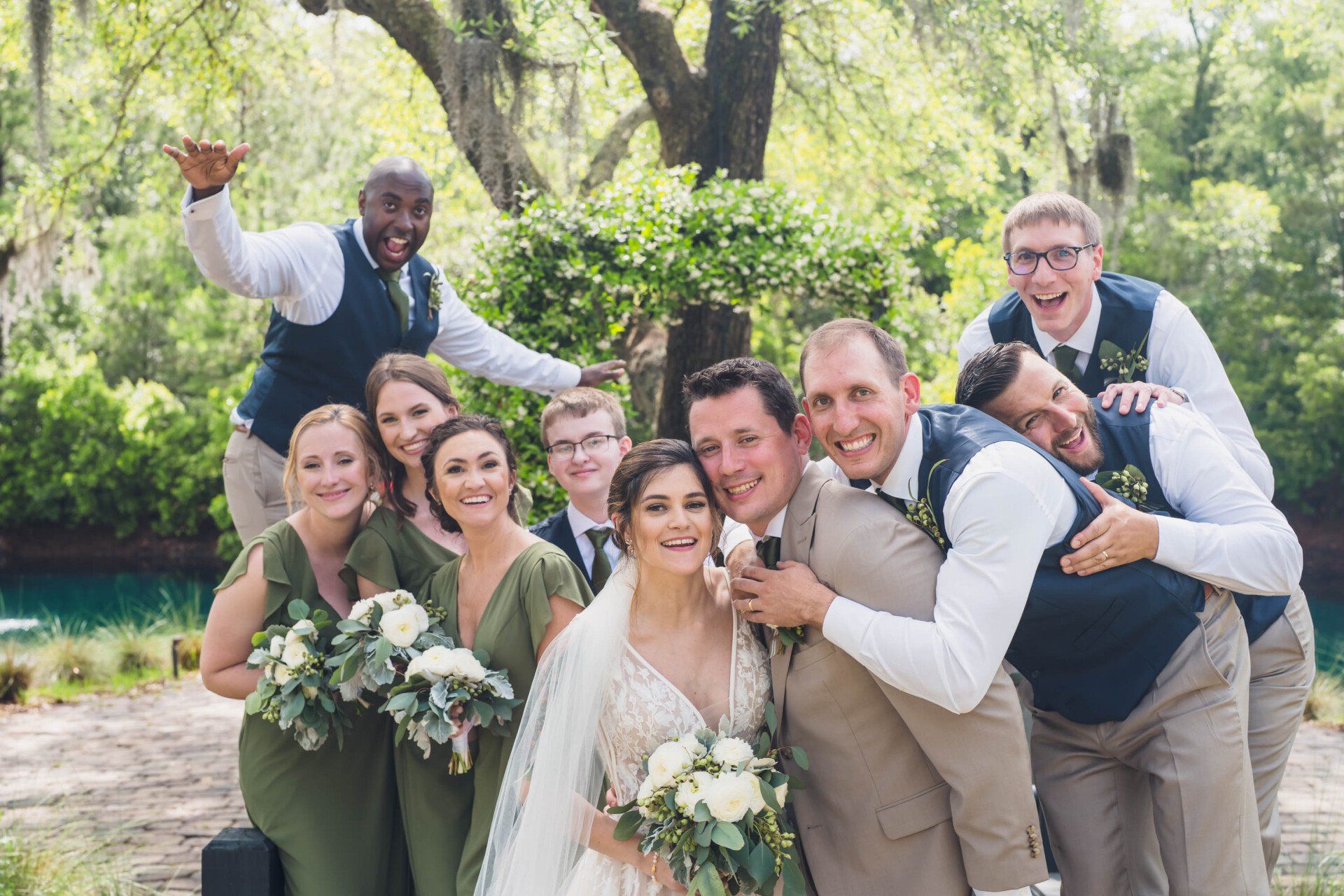 Wedding party posing outdoors, smiling and leaning together with bouquets and suits in a garden setting