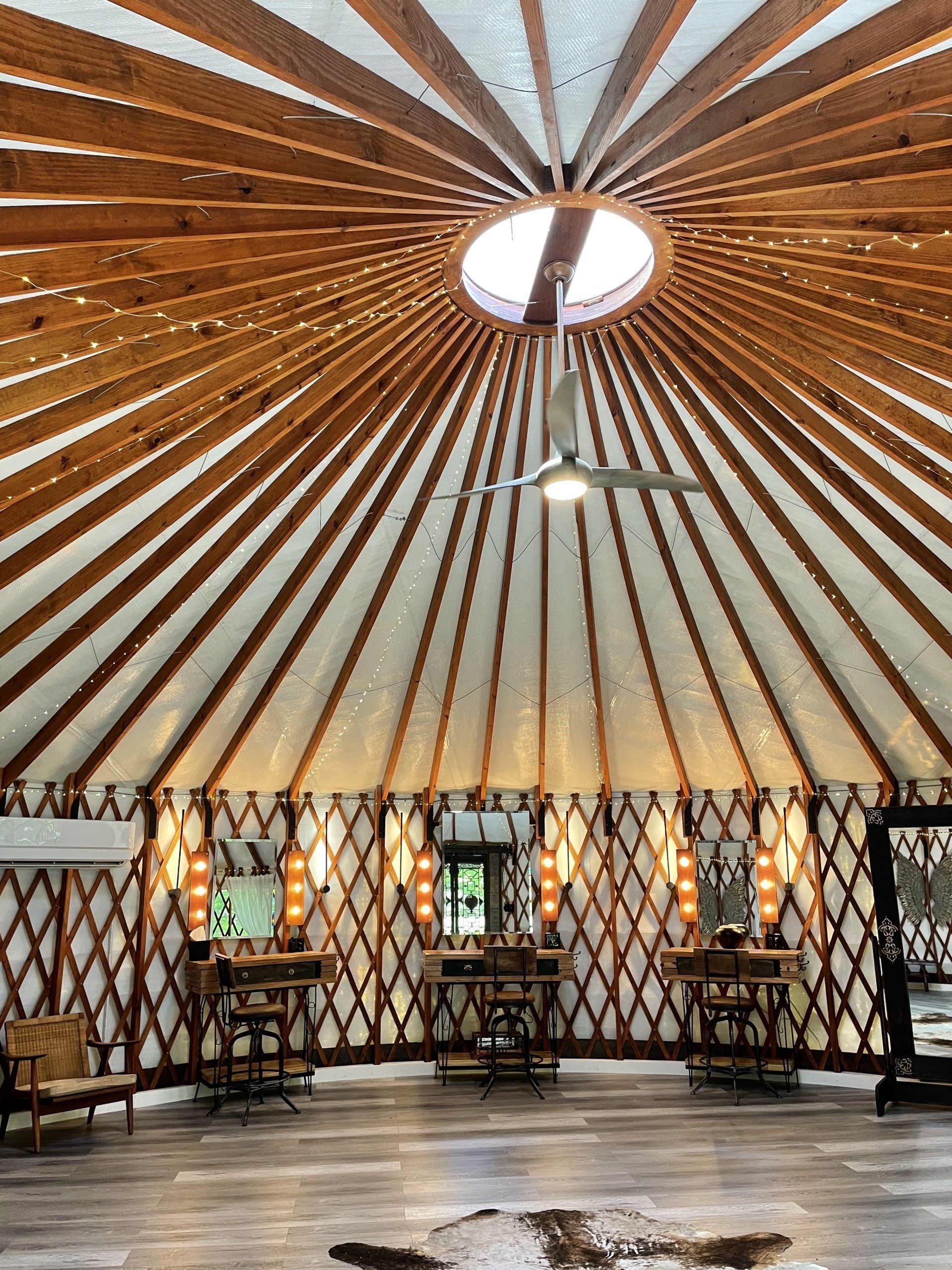 Interior of a circular yurt with wooden lattice walls, skylight, and tables around the perimeter.