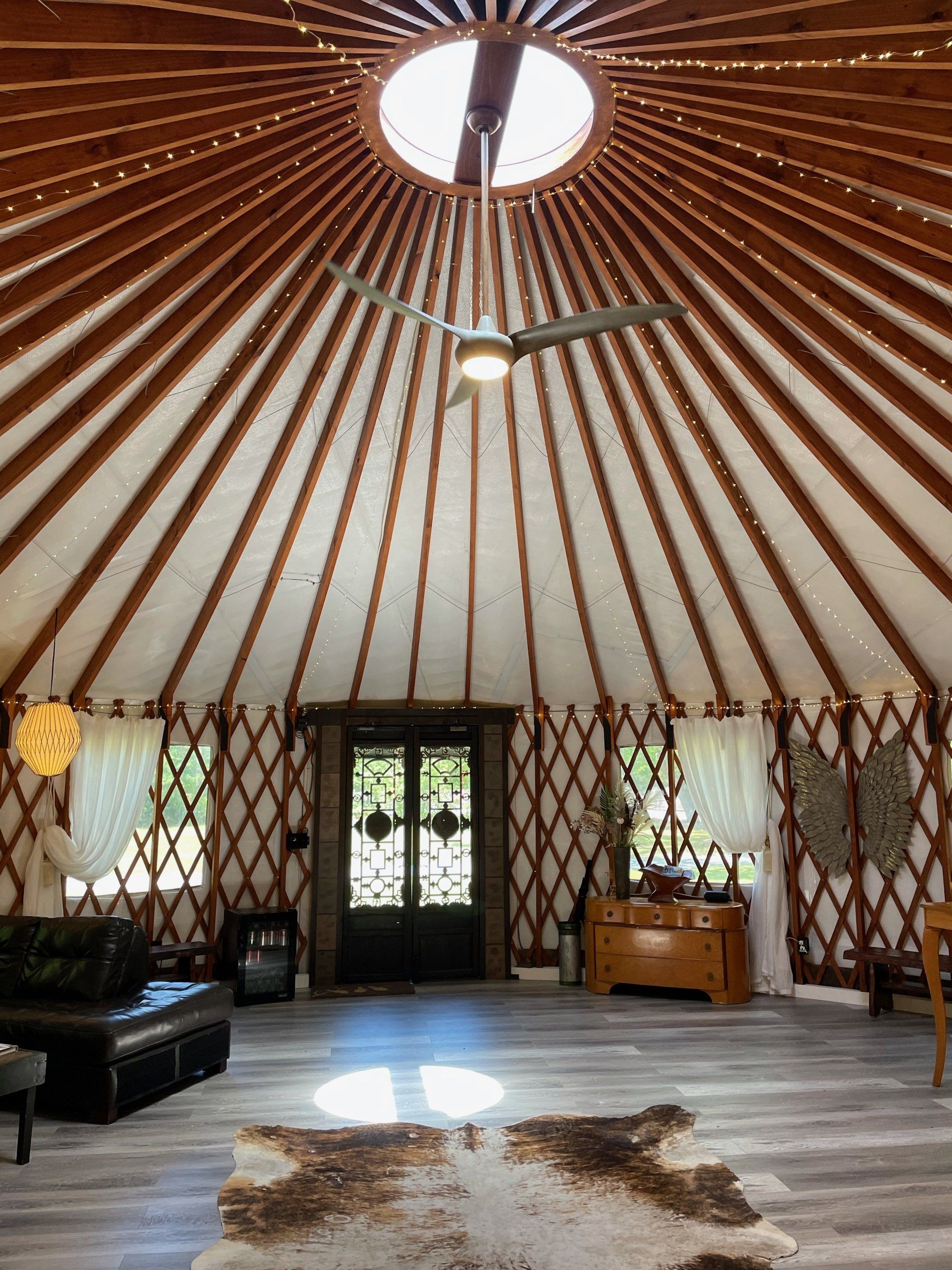 Round yurt interior with wooden lattice walls, skylight, ceiling fan, sofa, desk, and patterned rug