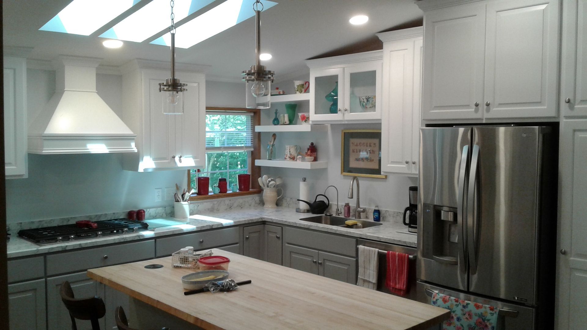 White and gray kitchen with a stainless steel refrigerator, island, and open shelves.
