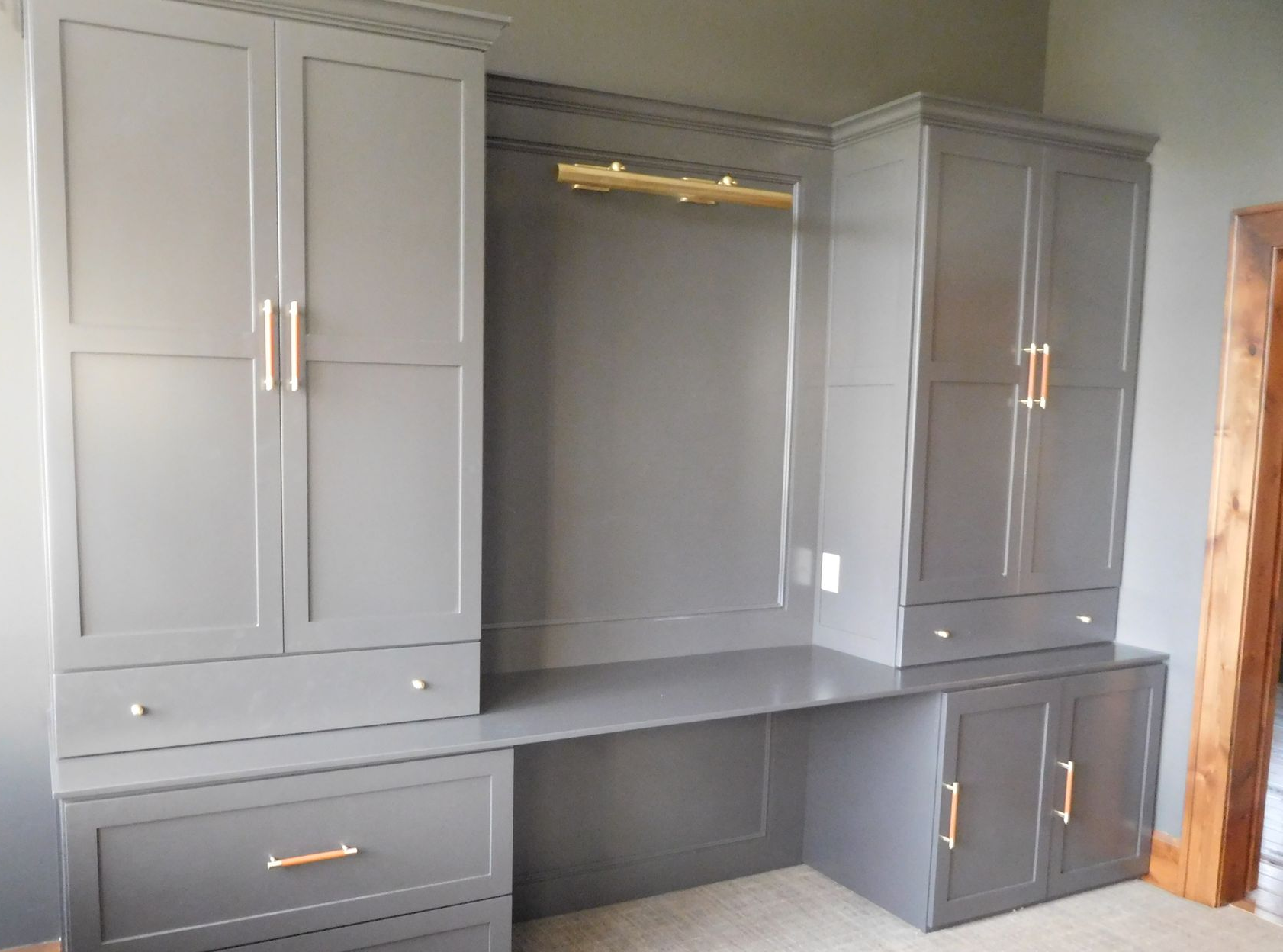 Gray built-in cabinets and desk with gold hardware and a hanging rod, in a room with a wooden beam.
