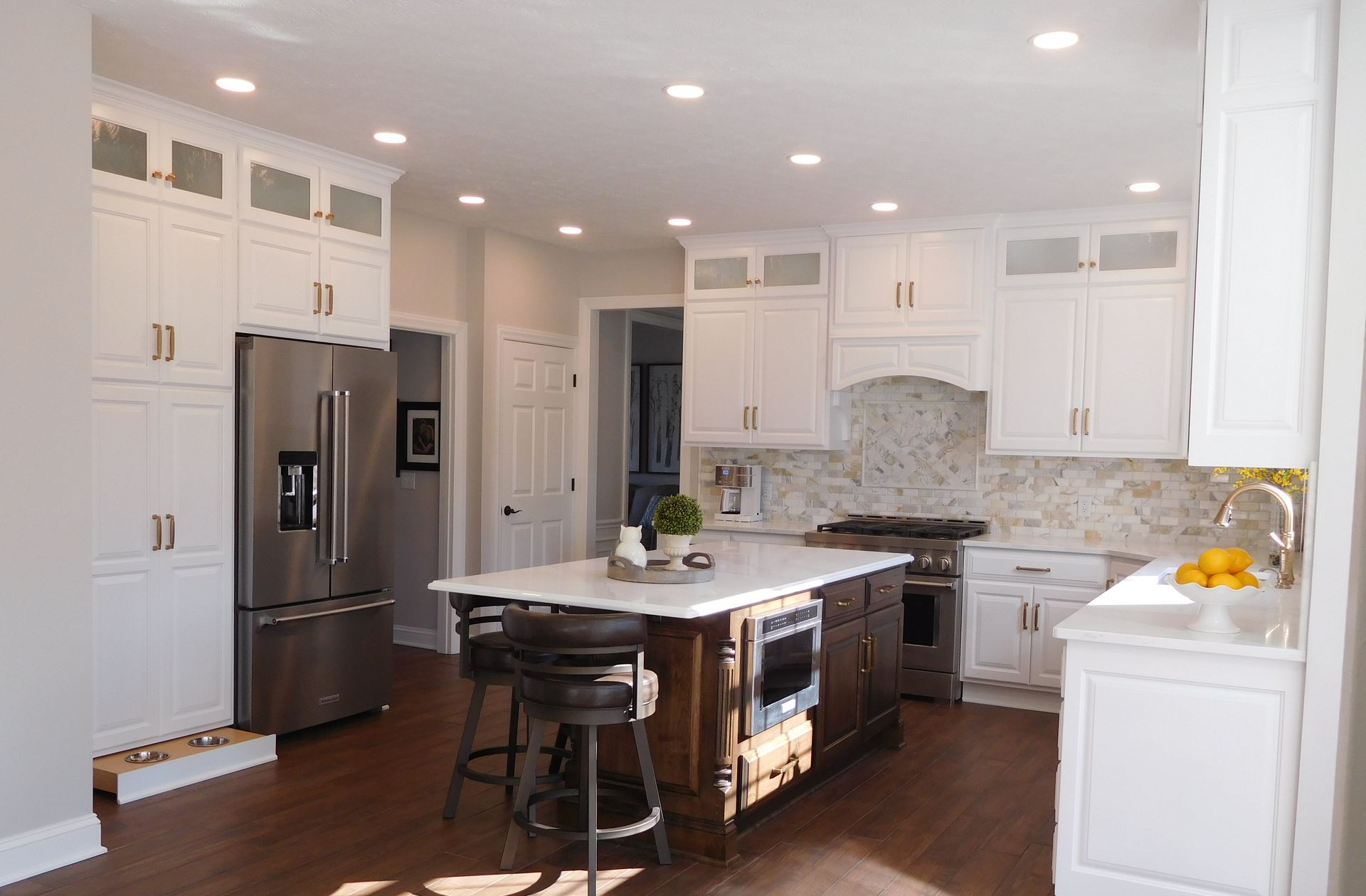 White kitchen with stainless steel appliances, dark wood island, and bar stools.