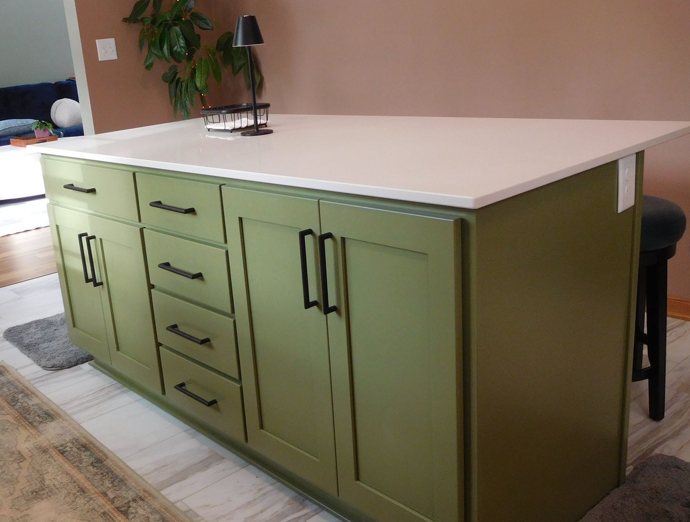 Green kitchen island with white countertop, black handles, and a small lamp.