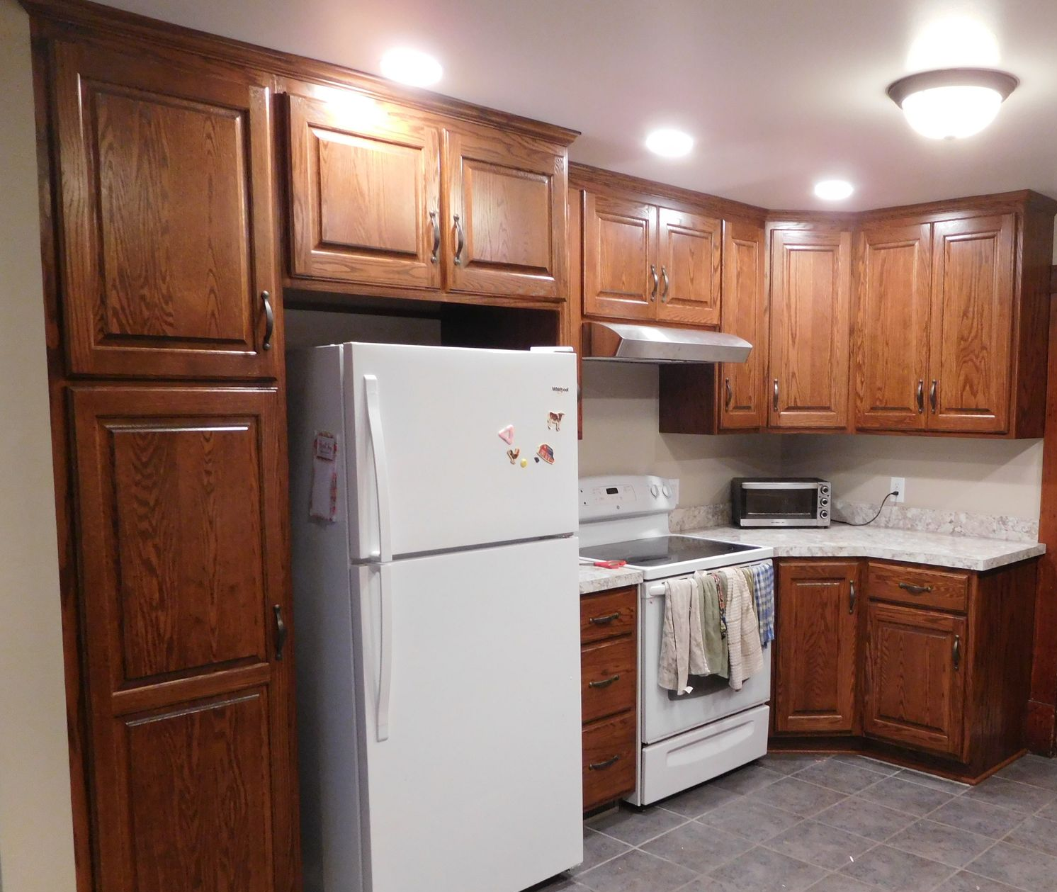 Kitchen with brown cabinets, white appliances, and gray tile floor.