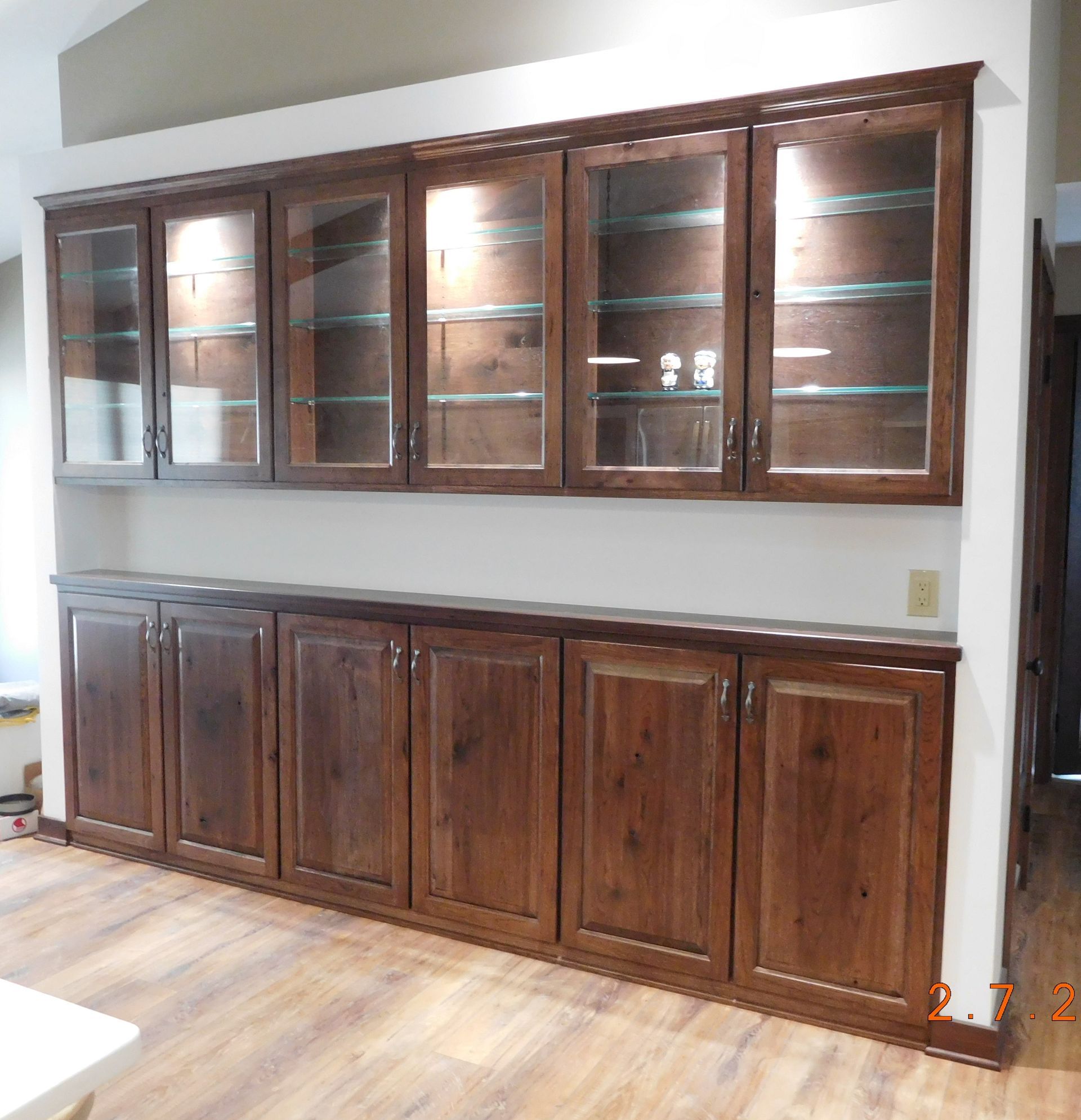 Built-in wooden cabinets with glass-front uppers and solid-door lowers, on a wall with wood flooring.