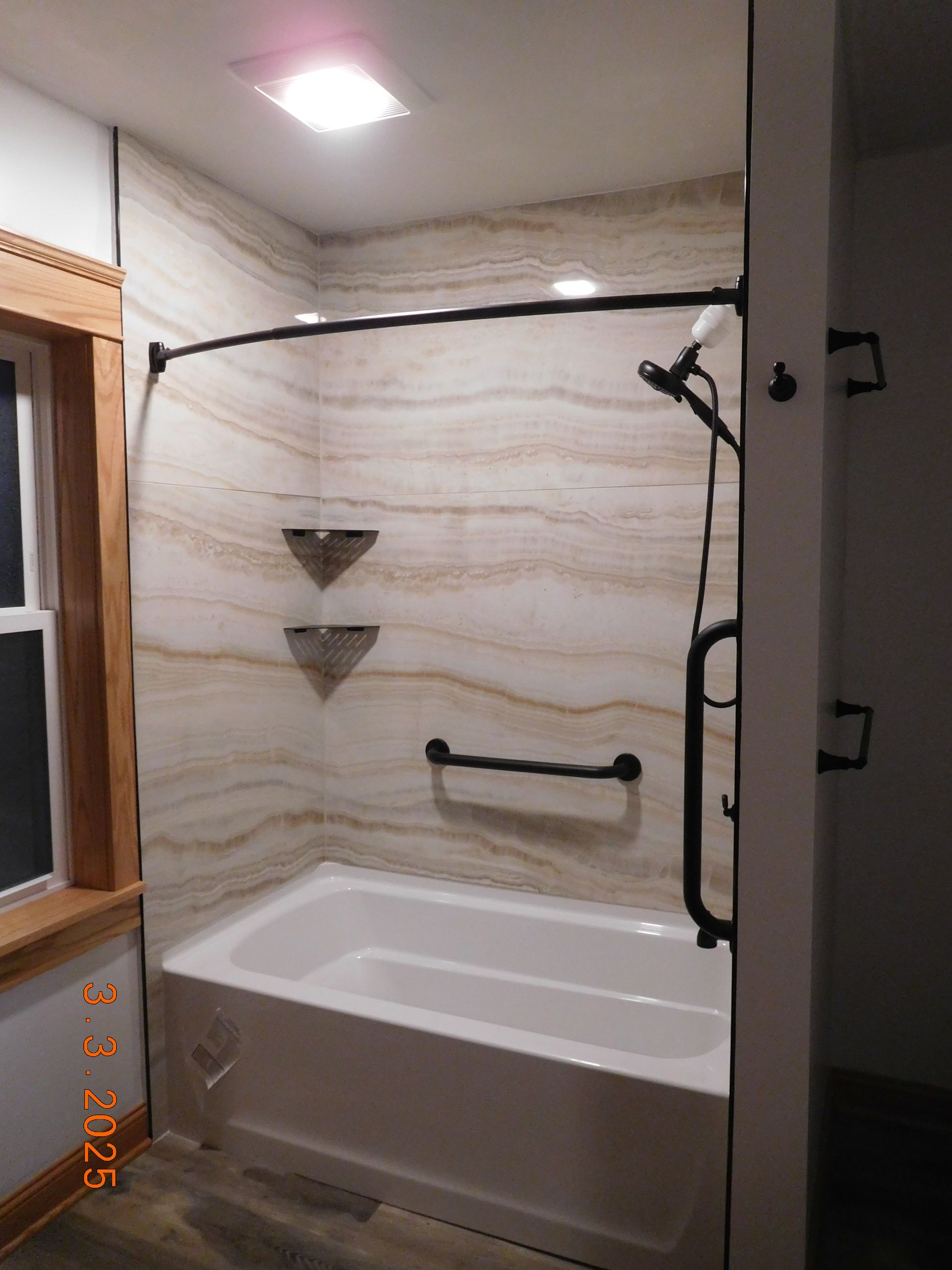 Bathroom with a white bathtub, beige patterned walls, black shower fixtures, and grab bar.
