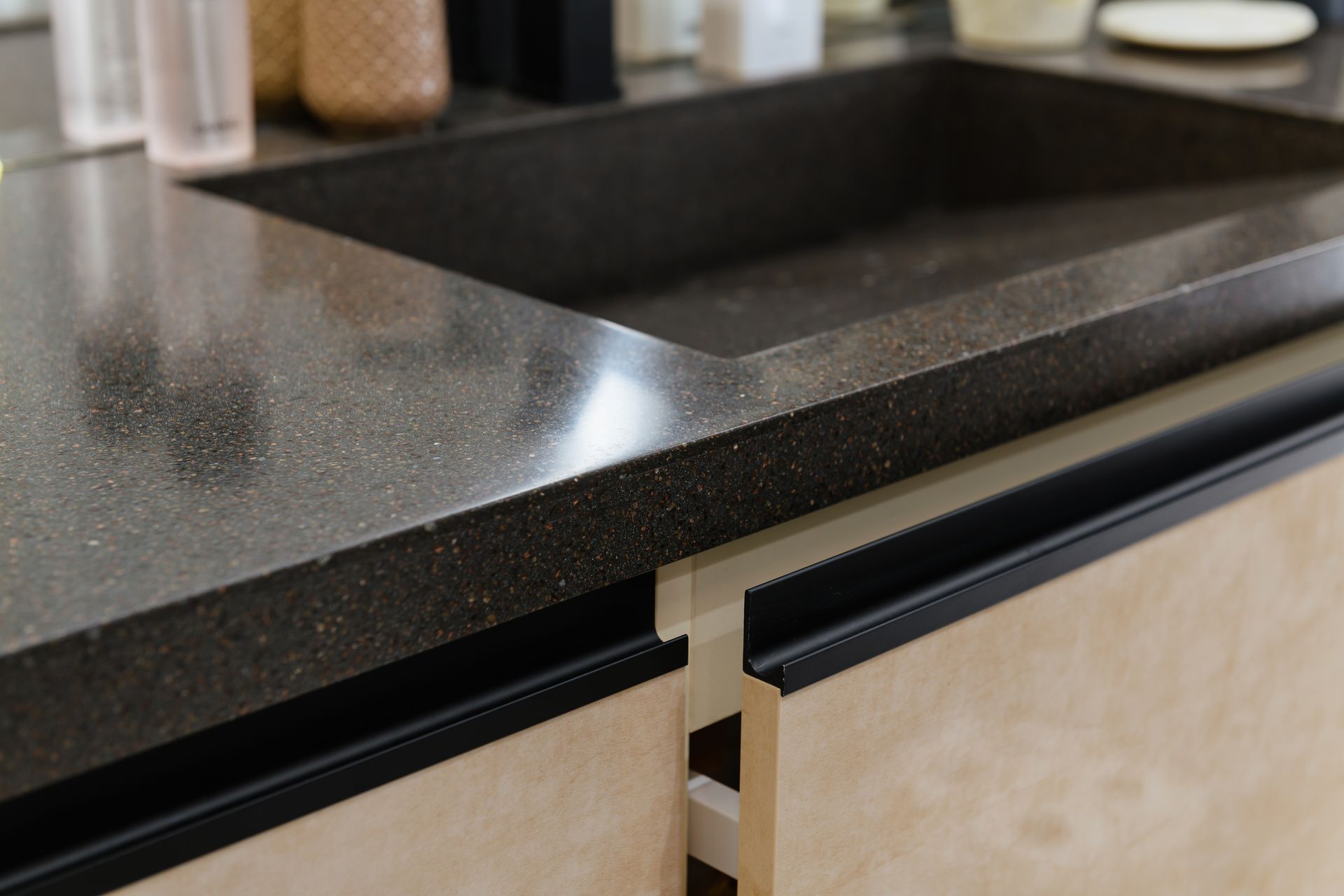 Dark countertop with integrated sink above light-colored cabinet with black handles; kitchen detail.