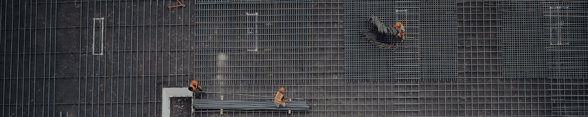 People working on a steel framework, seen from above with orange safety harnesses and tools on the grid.