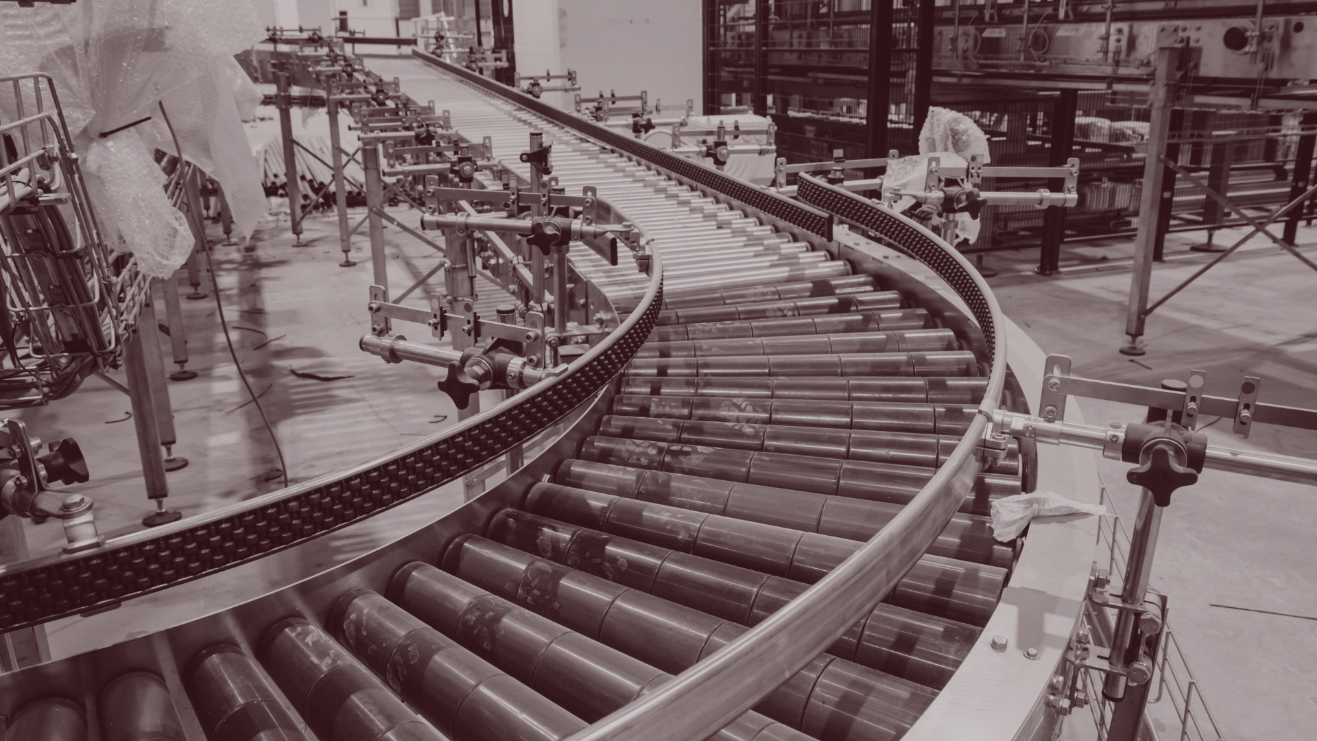 Curved roller conveyor in an industrial warehouse with metal frames and equipment nearby