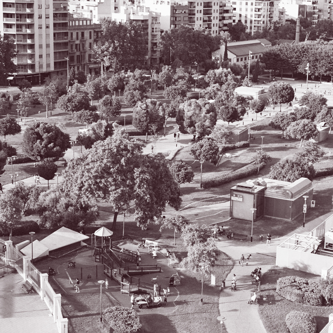 Aerial view of a park with trees, walking paths, benches, and nearby apartment buildings