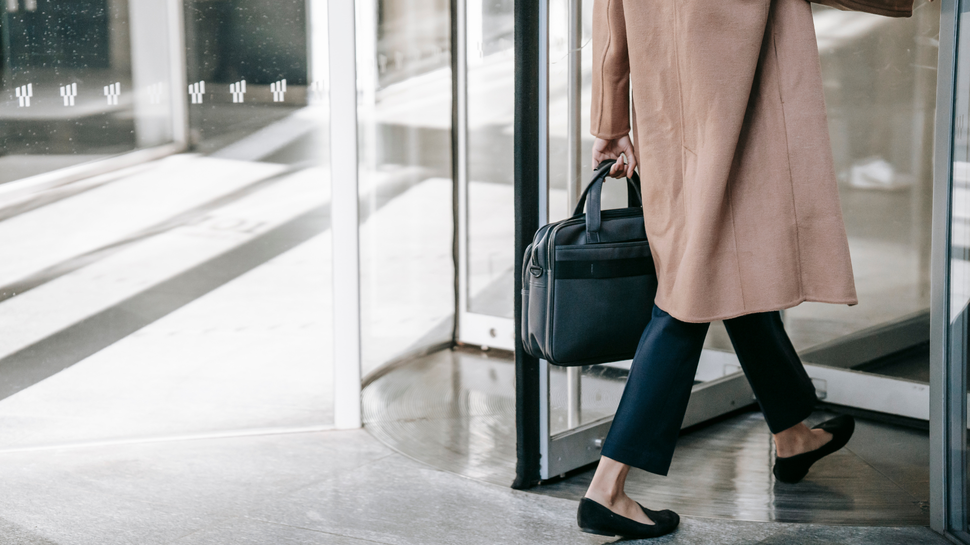 Person entering a building through a revolving door, carrying a black bag.