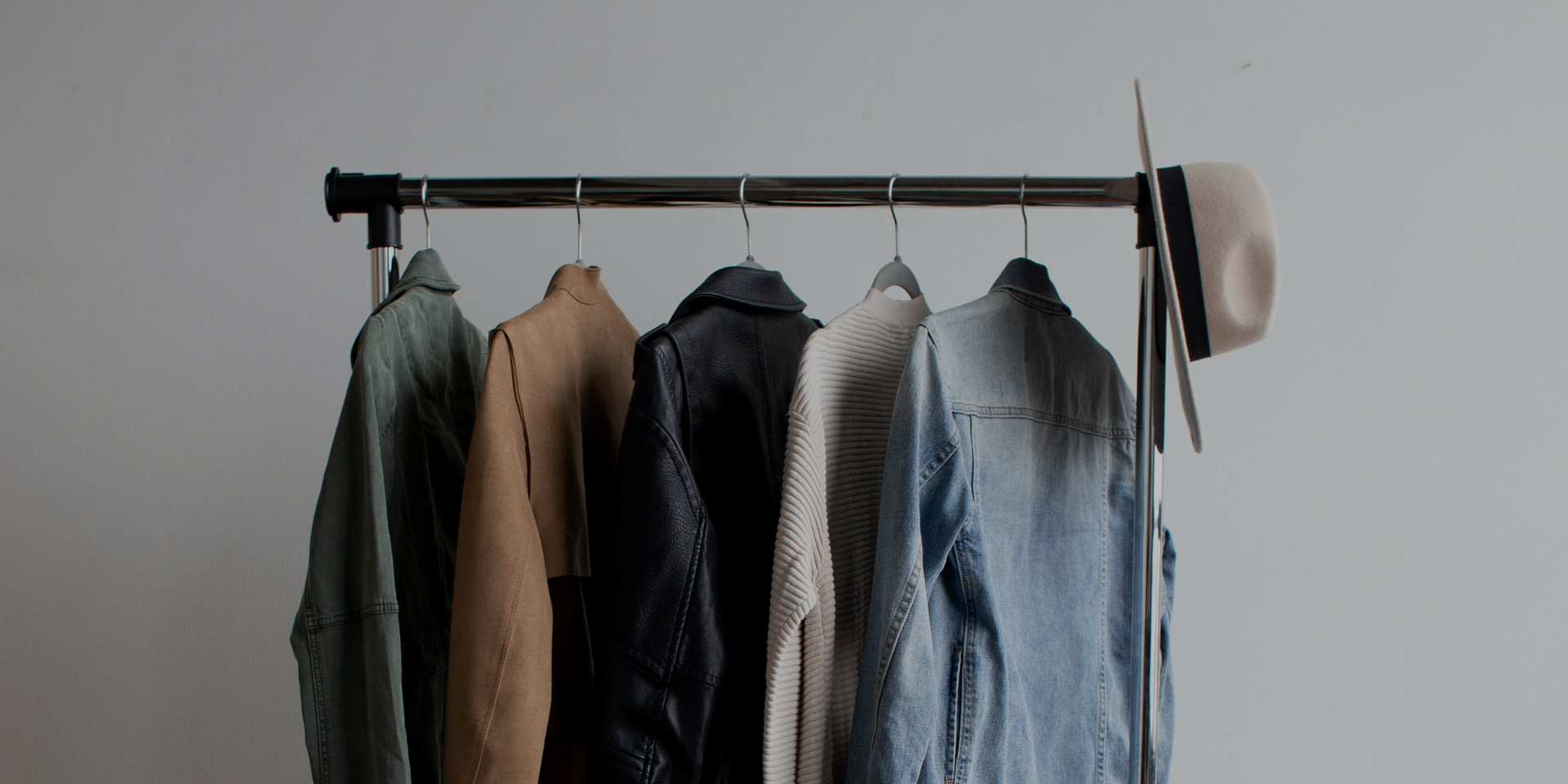 A row of clothes hanging on a rack with a hat hanging on the wall.