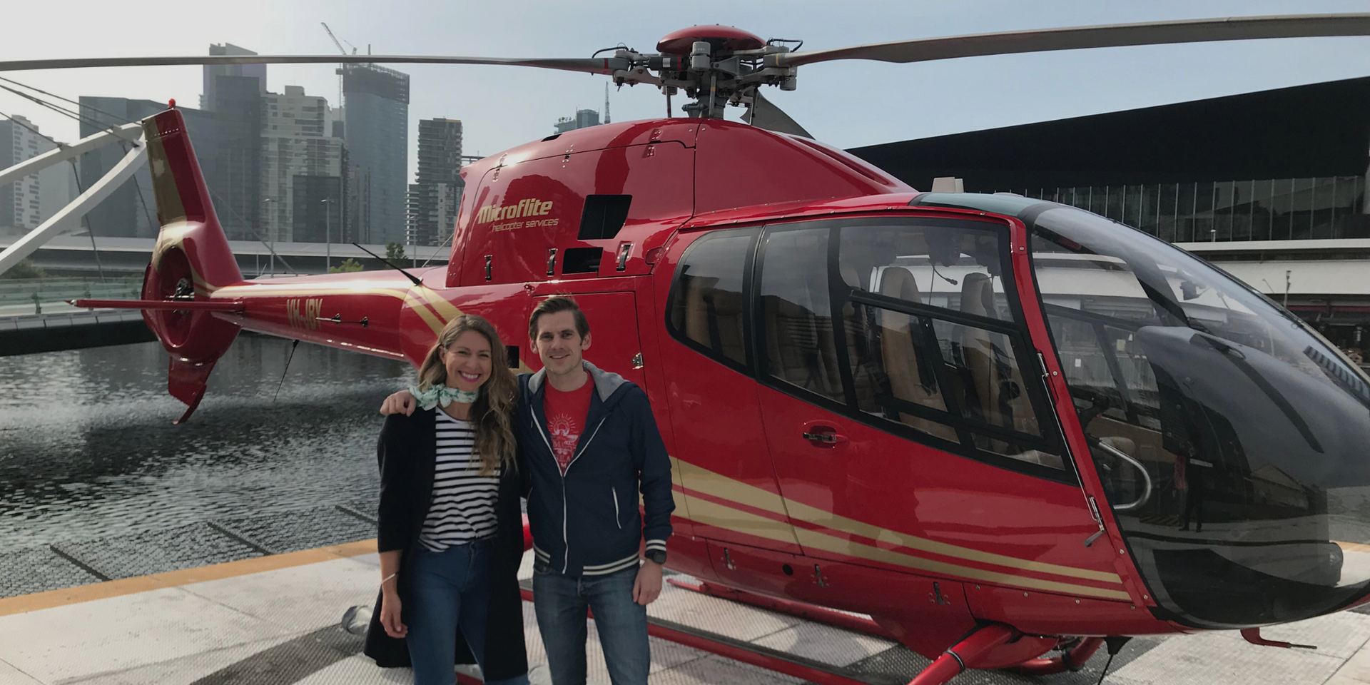 A man and a woman are standing in front of a red helicopter.