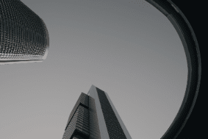 Looking up at modern skyscrapers framed by a circular opening against a gray sky