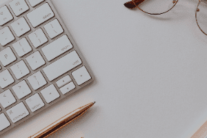 White keyboard and pencil on a minimalist desk with eyeglasses in the corner