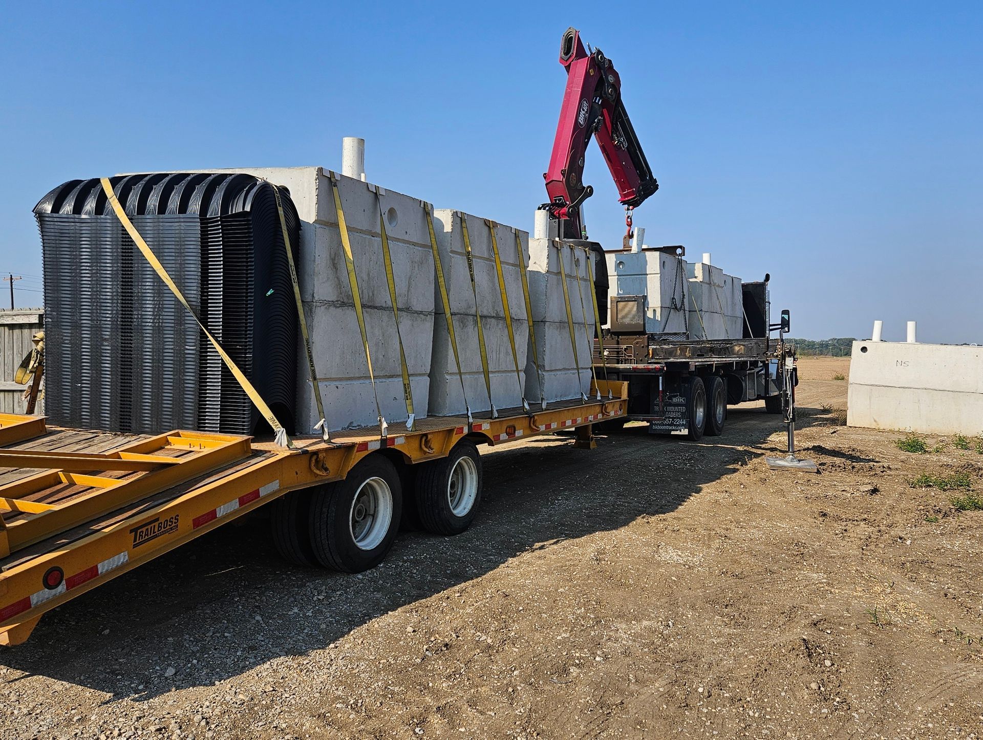 Three white Ford pickup trucks parked on a gravel lot, with a yellow excavator on a trailer nearby.