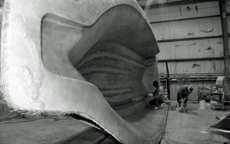 Huge sculptural fiberglass shell in a workshop with two people inspecting it.