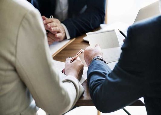 Three people in business attire discussing documents around a table