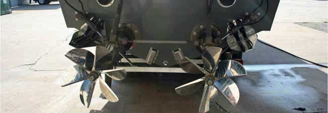 Close-up of a metallic aircraft or vehicle underside with four shiny landing gear struts on a concrete surface
