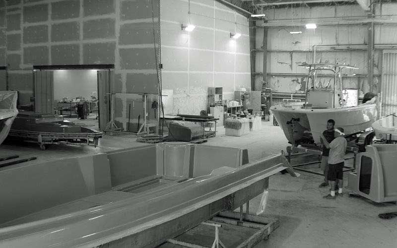 Large industrial workshop with boats, machinery, and two people working near a hull.
