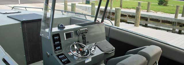 Boat cockpit with helm, throttle controls, and gray seats on a sunny marina dock