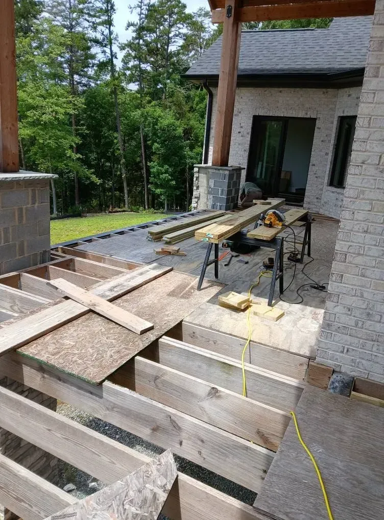 Gravel driveway under construction with a mini excavator and overcast sky beside a house and yard