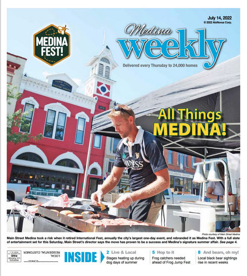 A man grills food at a booth in front of a red building on the cover of the Medina Weekly newspaper, dated July 14, 2022.