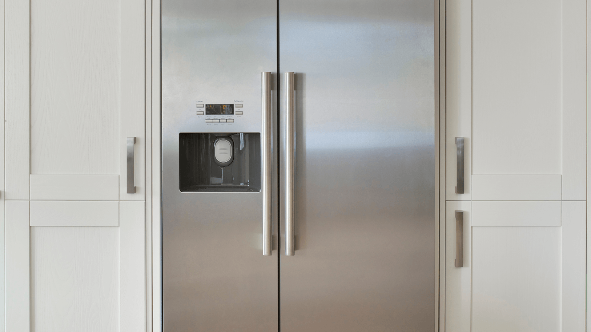 Stainless steel side-by-side refrigerator built into white cabinetry with silver handles.