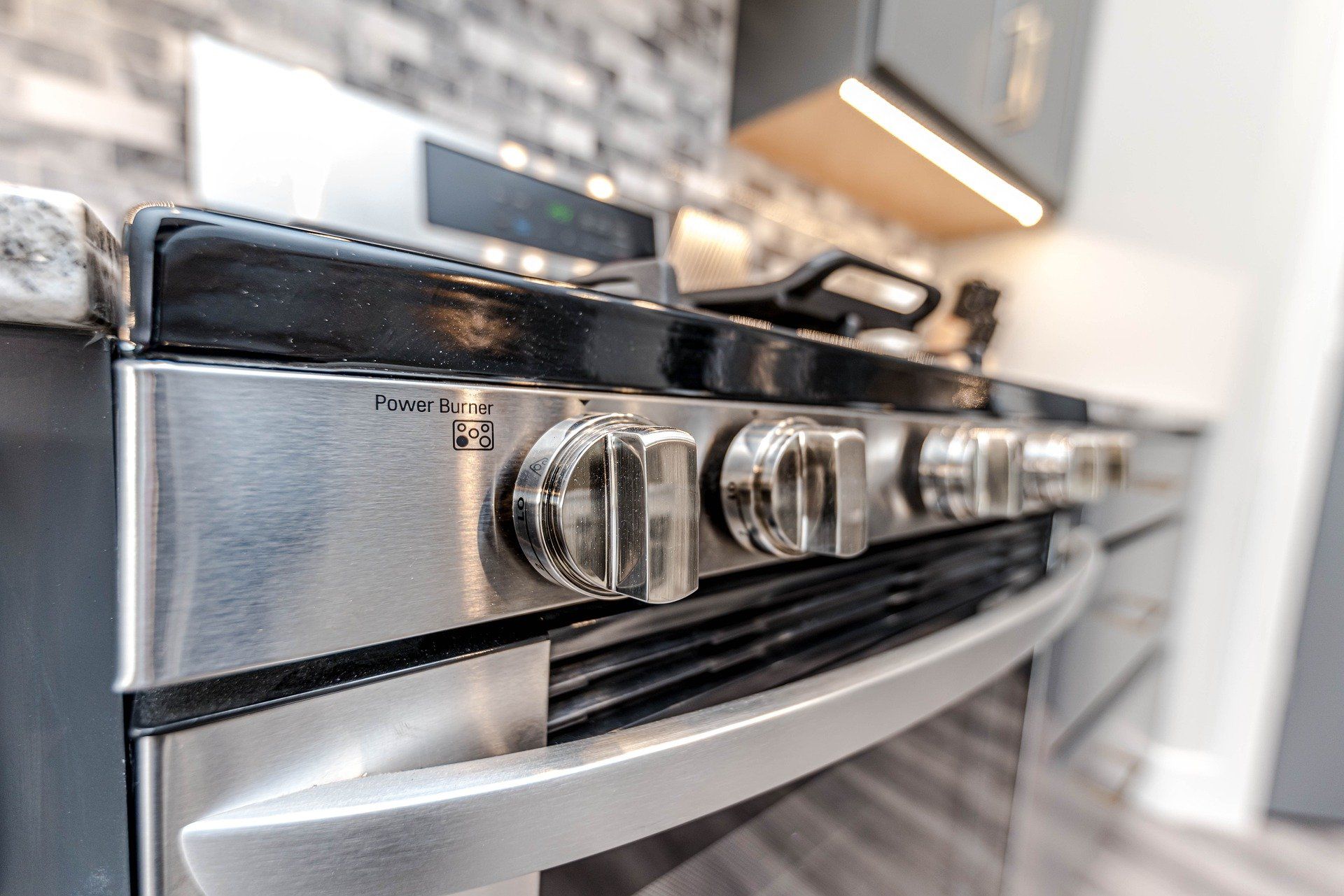 Stainless steel gas range with silver knobs, in a kitchen.